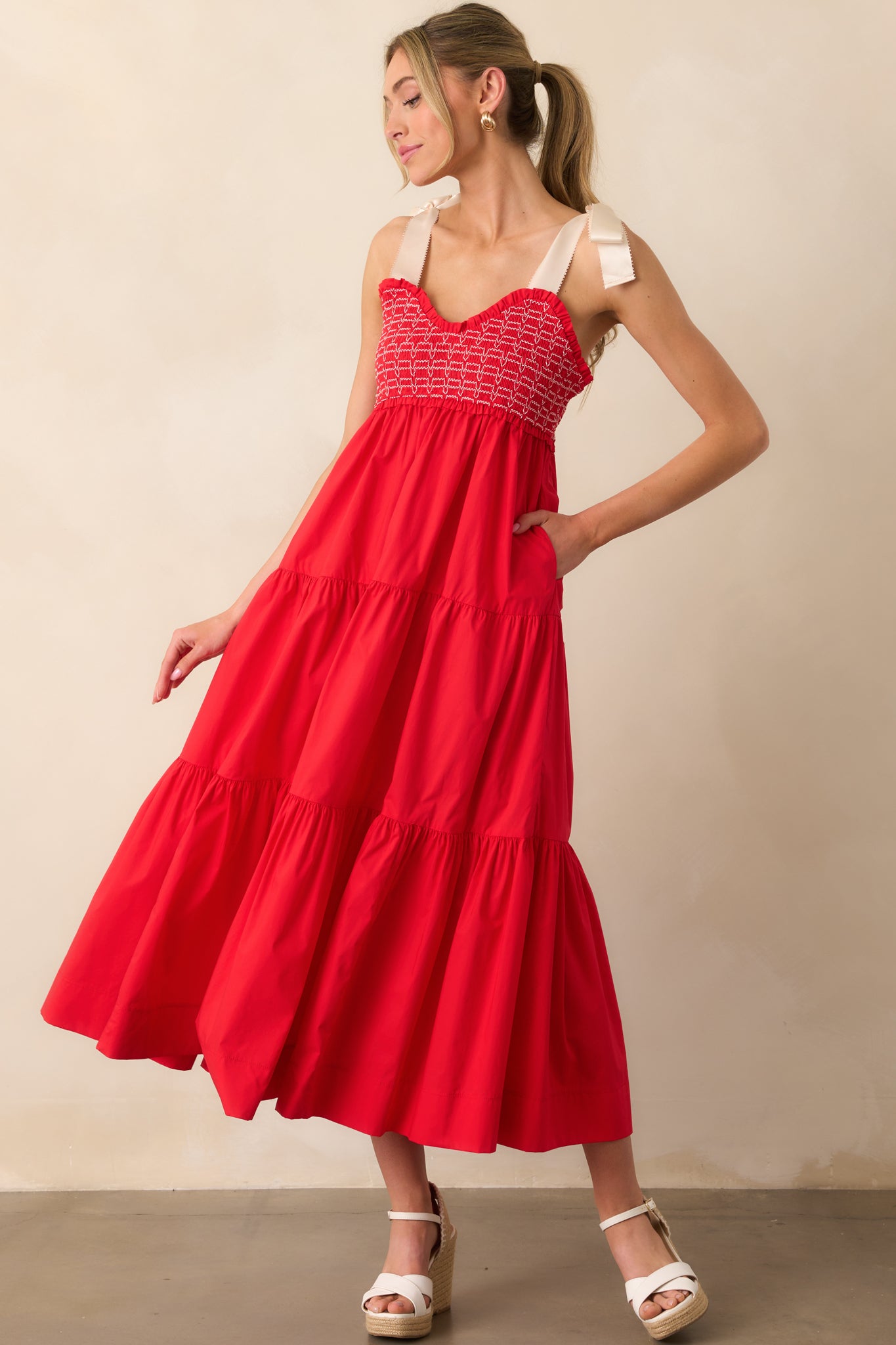 Action shot of a red maxi dress displaying the fit and movement, highlighting the v-neckline, thick self-tie straps, fully smocked bodice, functional hip pockets, and tiered design.