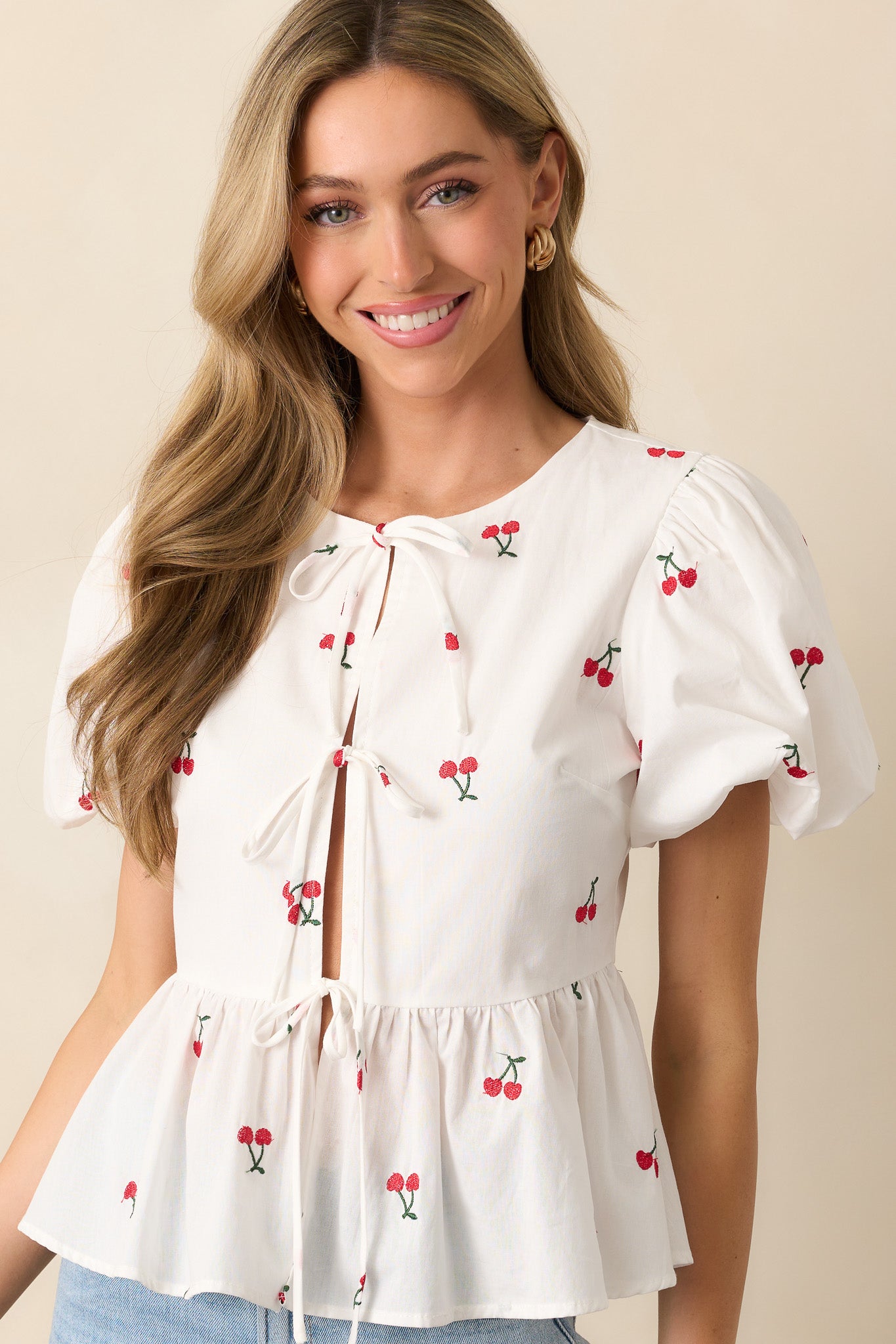 Embroidered cherry icons dance across this white top, highlighted by three self-tie bows at the center and soft puff sleeves.