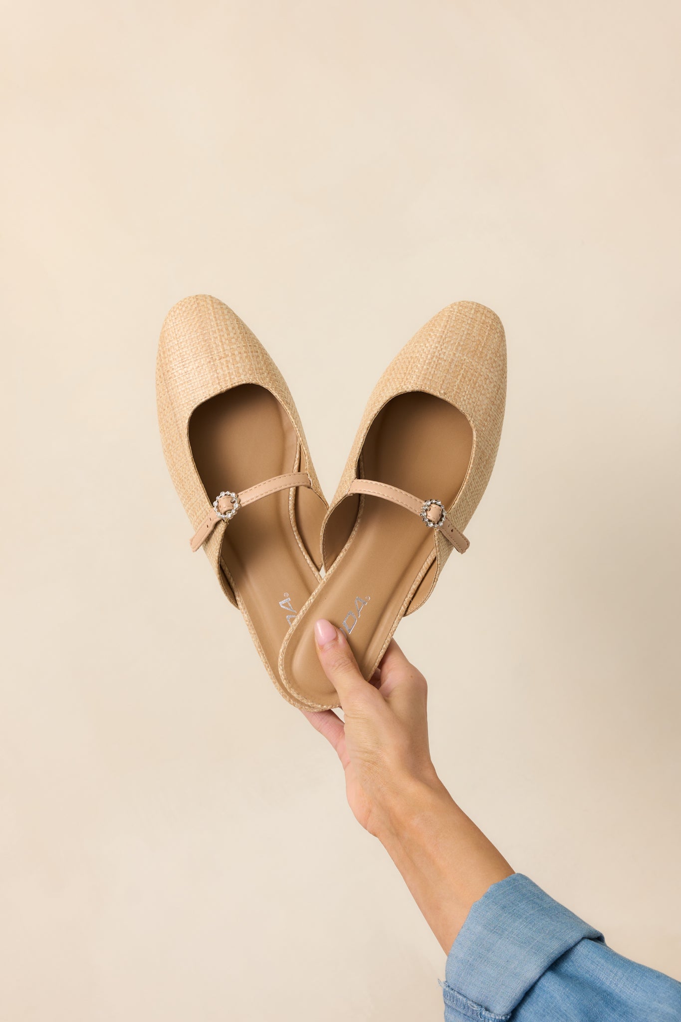 A woven raffia flat with a rounded toe and an adjustable buckle strap across the foot.
