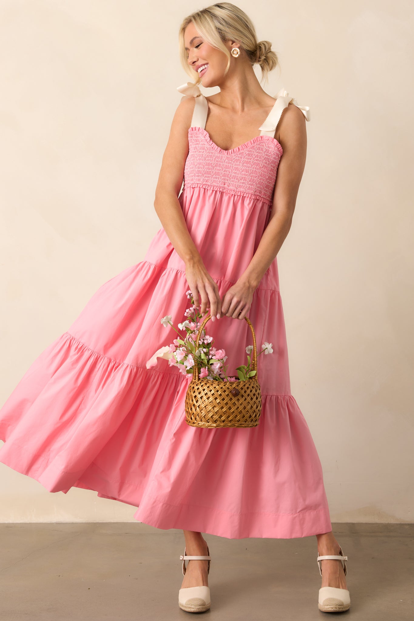 A pink coral midi dress with a sweetheart neckline, a fully smocked bust adorned with white embroidered detailing, ivory self-tie bow straps, and functional pockets.