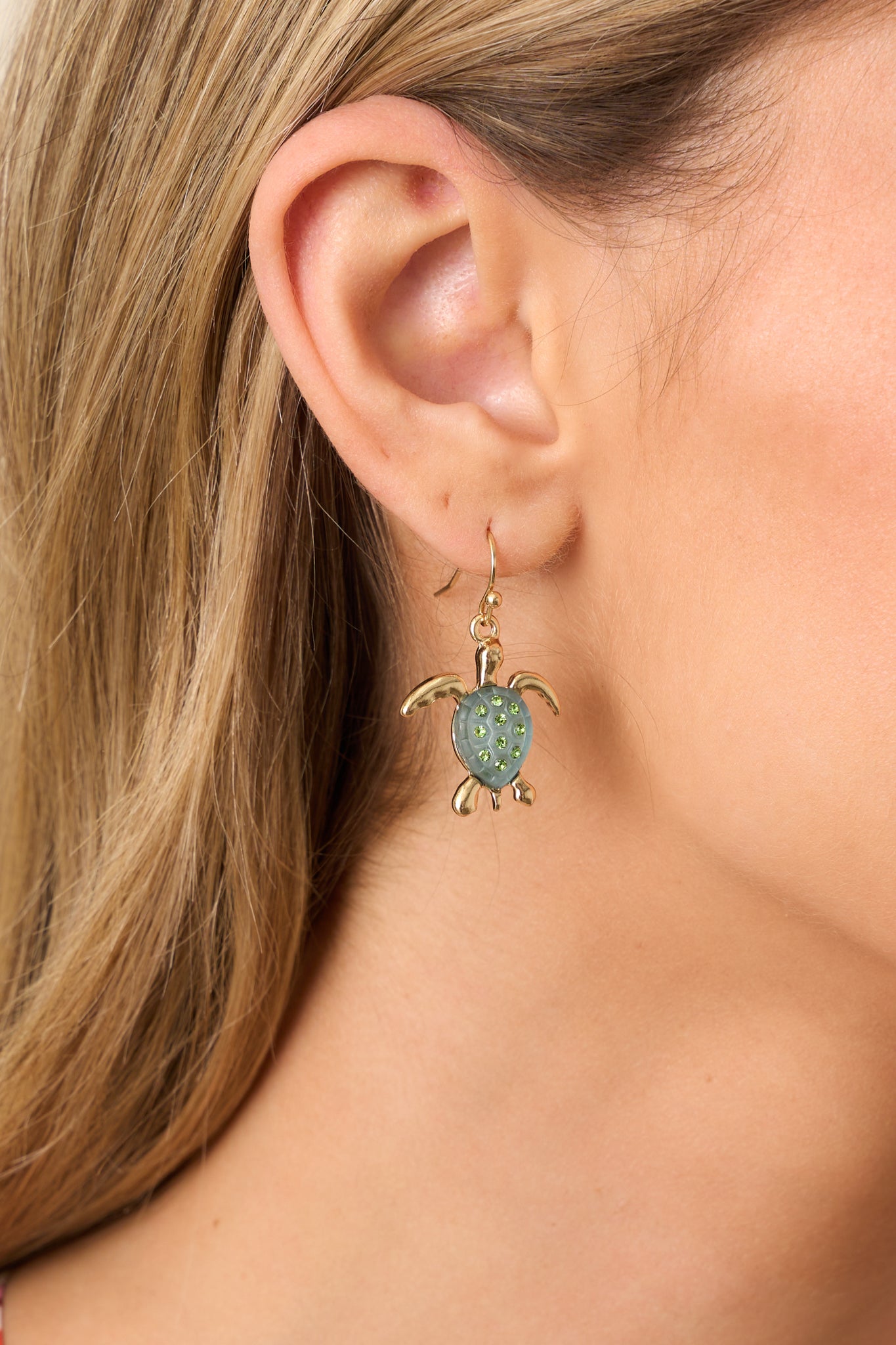 A close-up view of the gold turtle earring featuring its dangle design, intricate detailing, and rich green rhinestones.