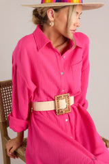 This pink dress features a collared neckline, functional buttons down the front, a front pocket on the left side of the bust, long sleeves with a cuff secured by a functional button, and two slits up the bottom hemline ending just below the knee.