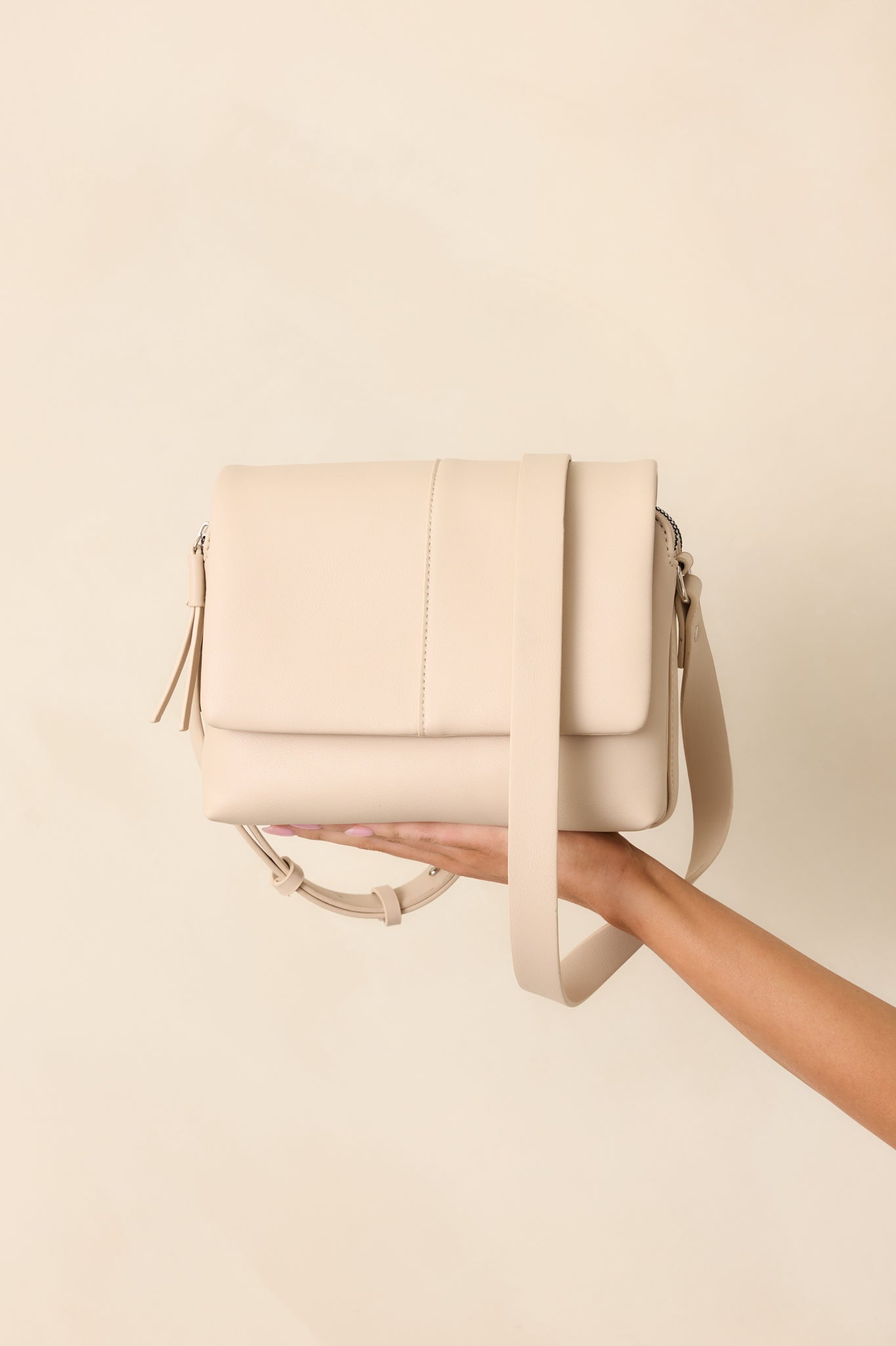 A full-length image of the light beige handbag with a magnetic flap closure and tassel zipper accents, fully displayed to show overall size and design.
