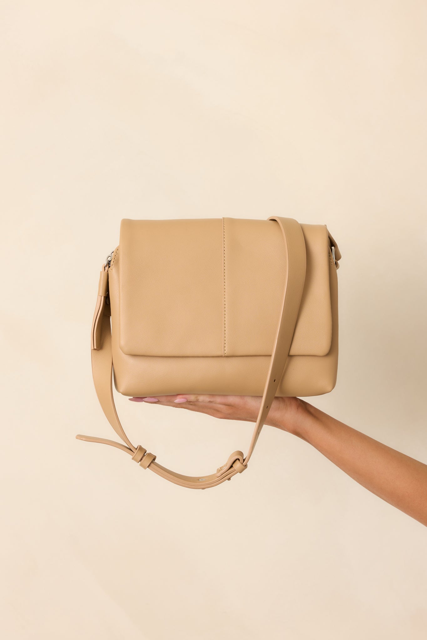 A complete profile view of the tan handbag with its flap magnetic closure and tassel zipper accents.