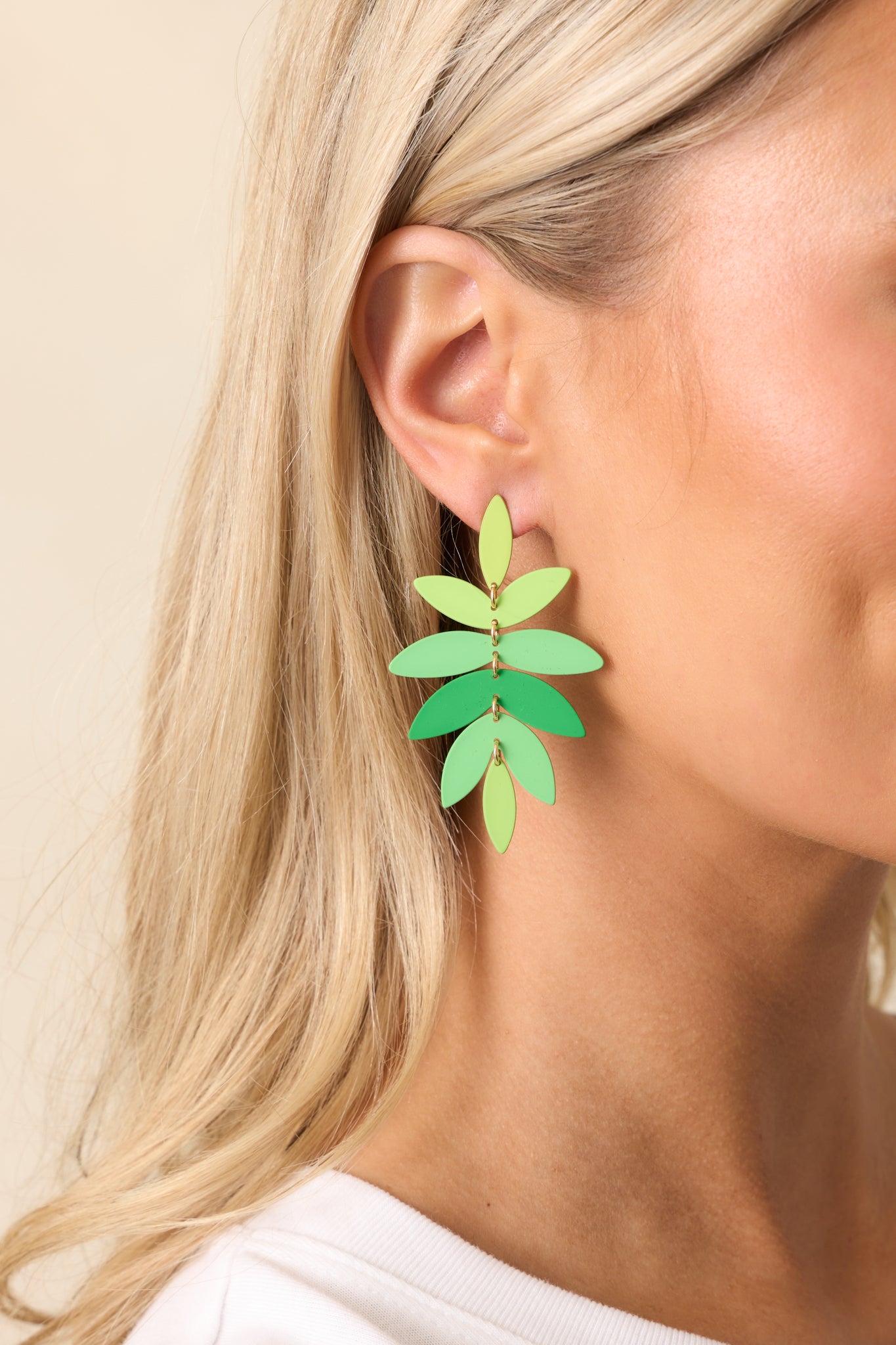 Partial view of one earring showing the curved palm leaf shape and a subtle green gradient design.