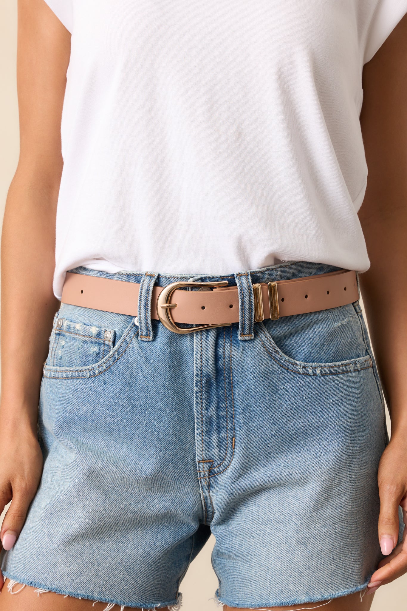 Cropped view of the beige belt styled at the waist, showcasing the gold buckle and smooth finish.