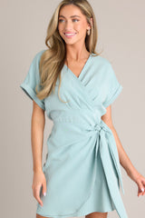 This green dress features a v-neckline, an elastic waist insert, a self-tie wrap feature, and wide cuffed short sleeves.