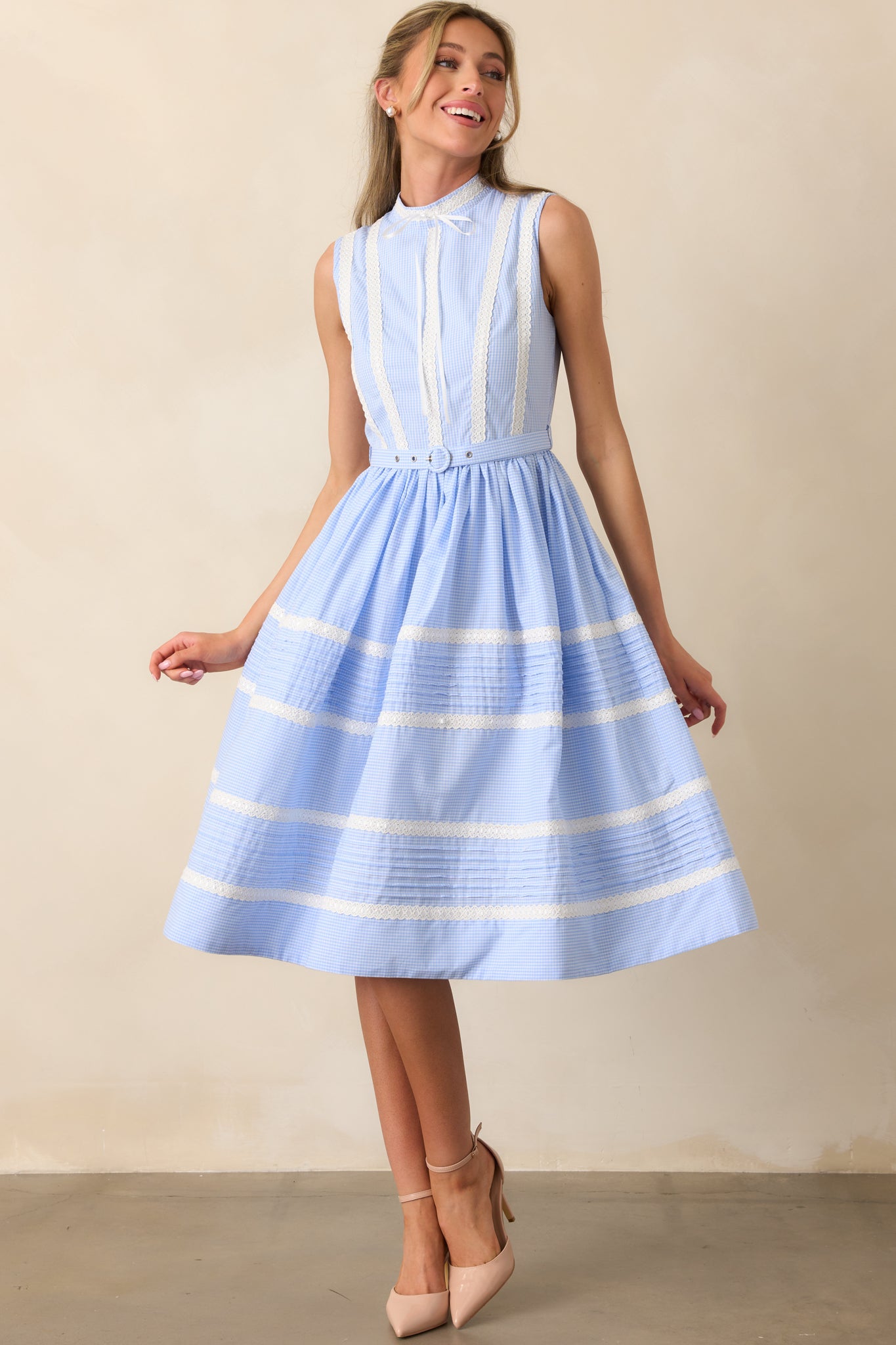 A blue midi dress featuring a mock neckline with a center bow detail, lace ribbon rows throughout, and a micro-gingham print.