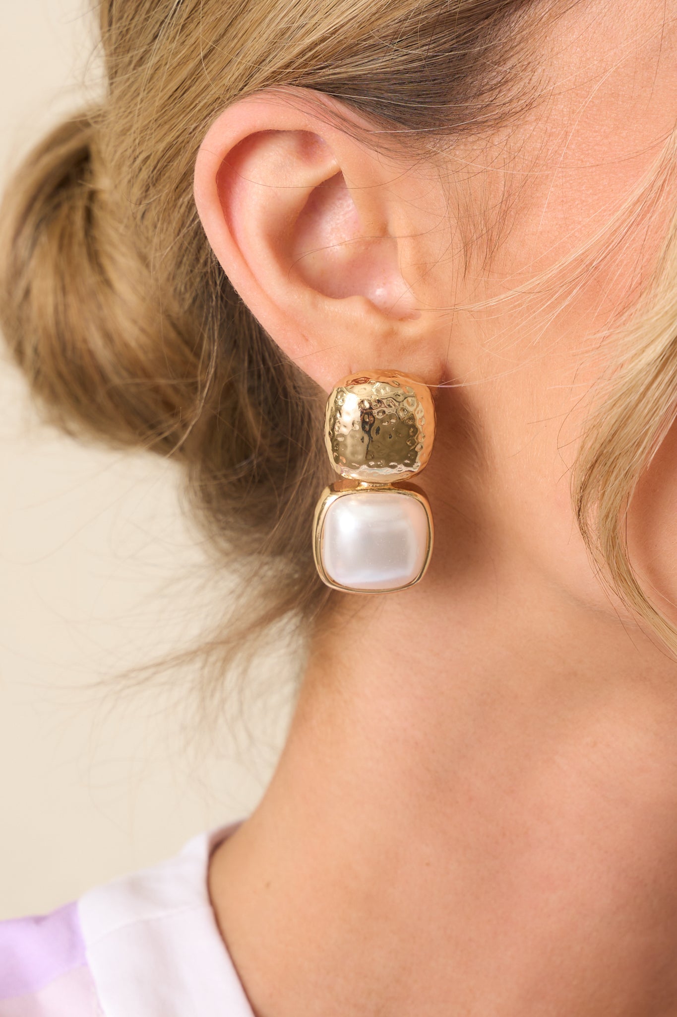 Extreme close-up of an earring’s gold stud and ivory faux pearl drop, focusing on the texture and secure back posting.