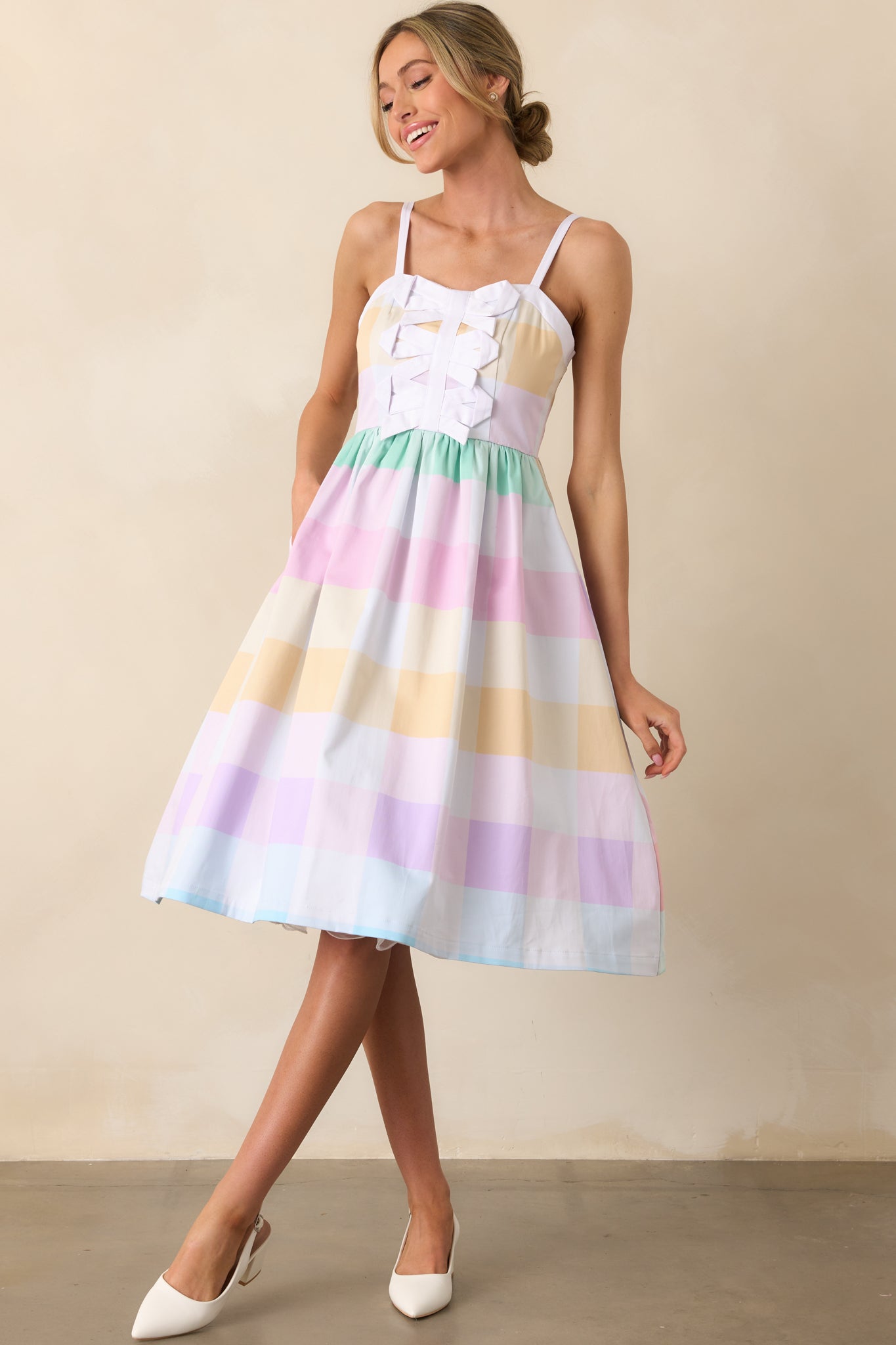 A midi dress featuring a pastel multicolor large gingham print, a sweetheart neckline, and three decorative bows down the center bodice.