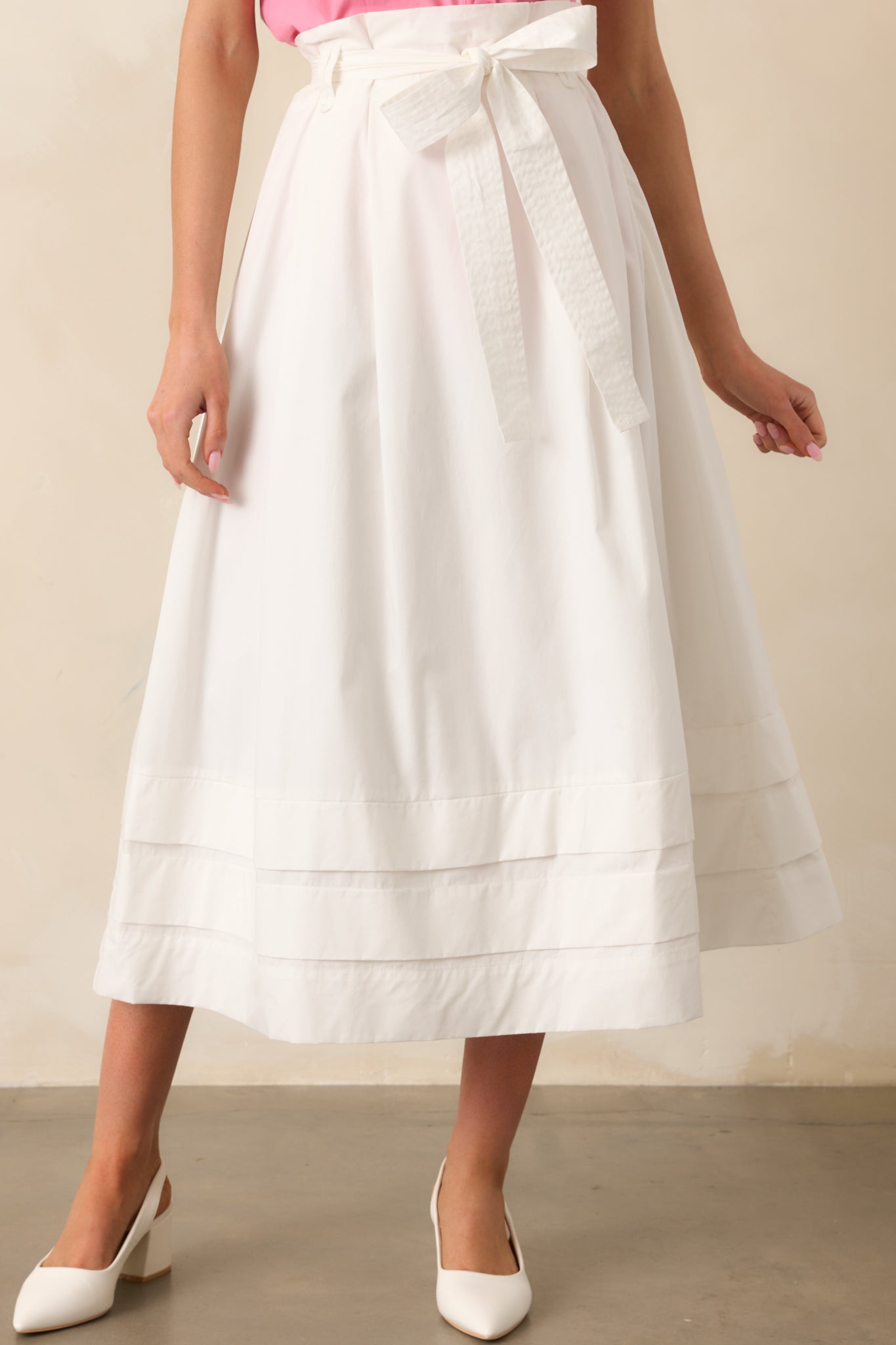 A focused look at the small tiers at the bottom of the white midi skirt, emphasizing the subtle layers and soft texture of the fabric.