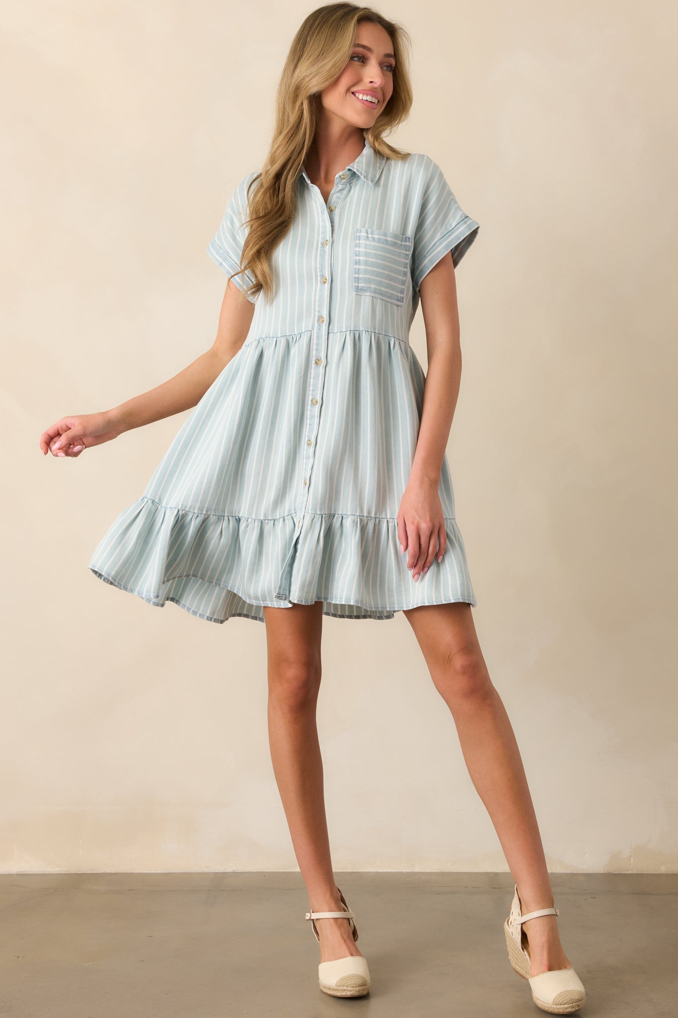 A chambray stripe mini dress featuring a collared high neckline, functional button front, and a tiered silhouette.