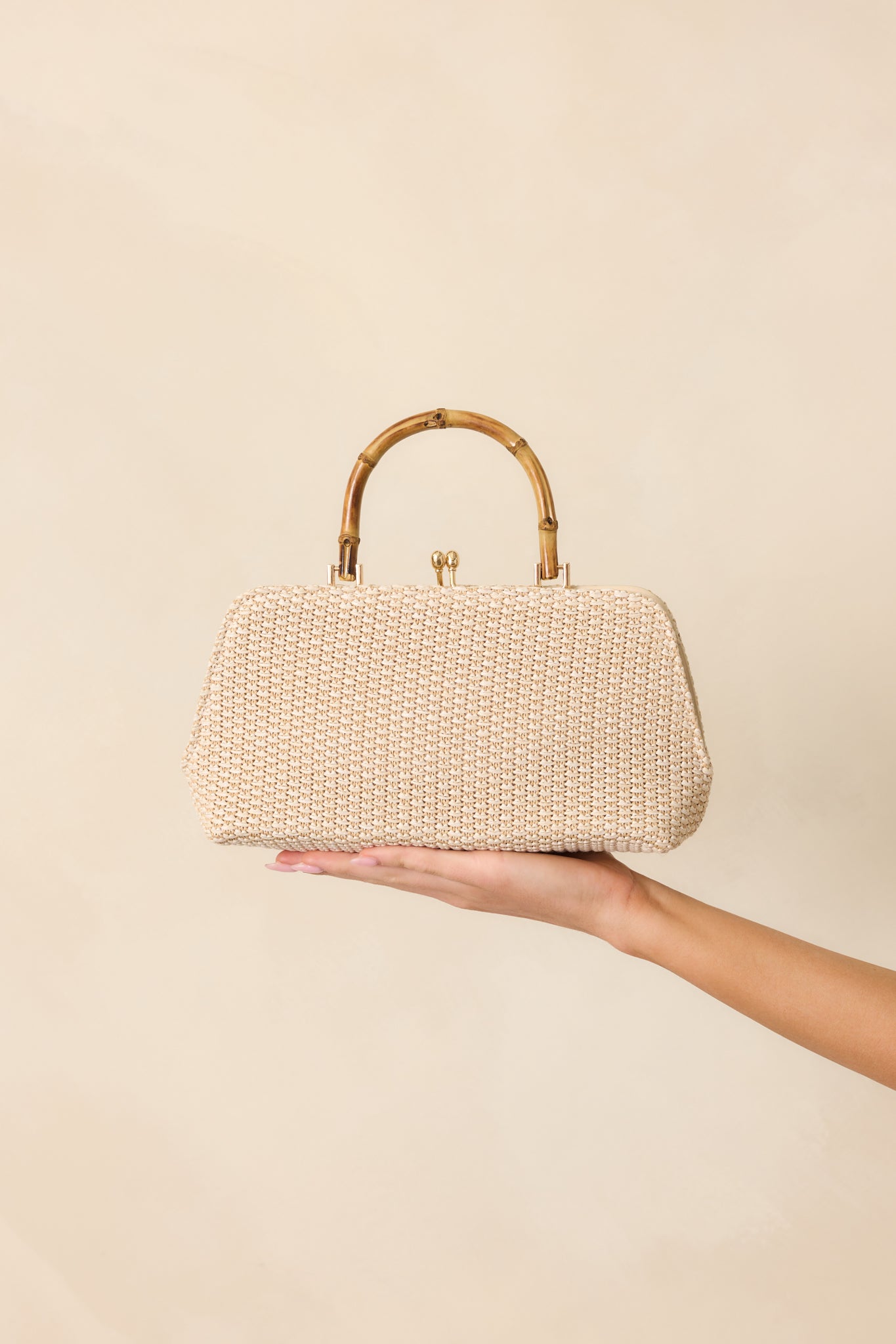 Full view of the ivory woven handbag featuring a structured brown bamboo handle and gold kiss lock clasp closure.