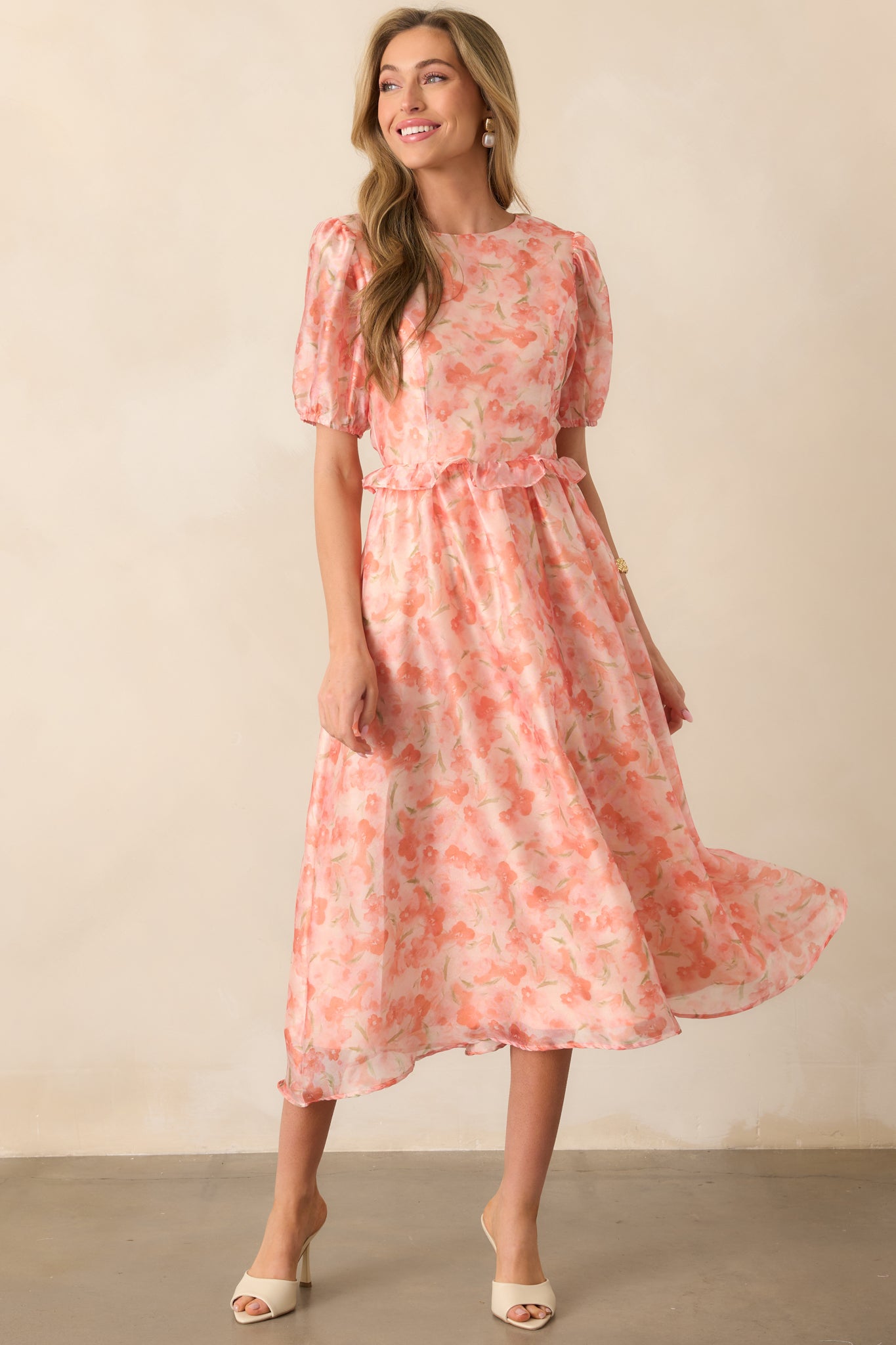 A light orange floral midi dress with short puff sleeves, a round neckline, and a ruffle waist. The flowing silhouette enhances the delicate floral print.
