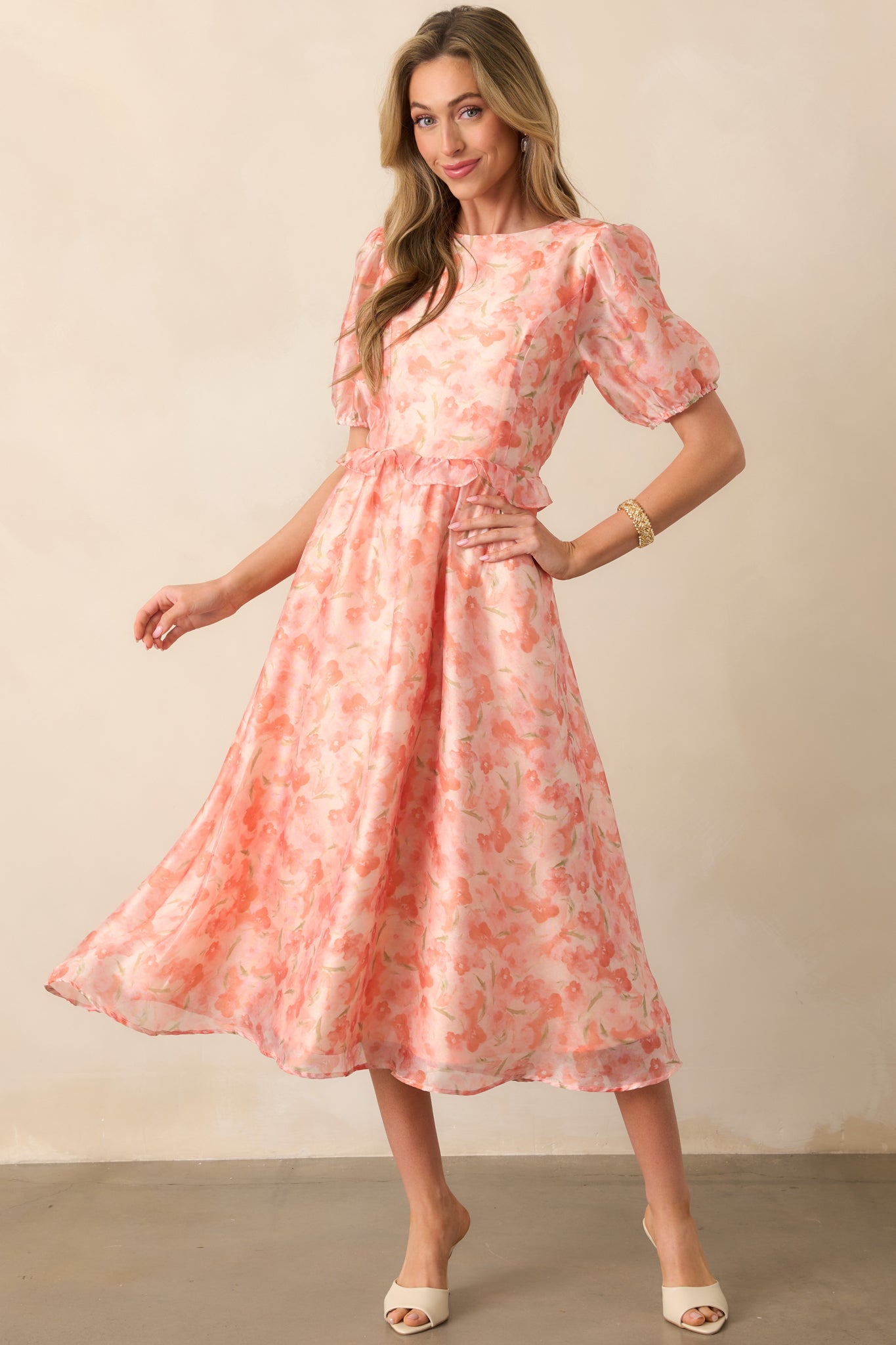 A floral midi dress with airy puff sleeves, a softly cinched waist, and a flowing skirt. The light orange print complements the graceful movement of the fabric.