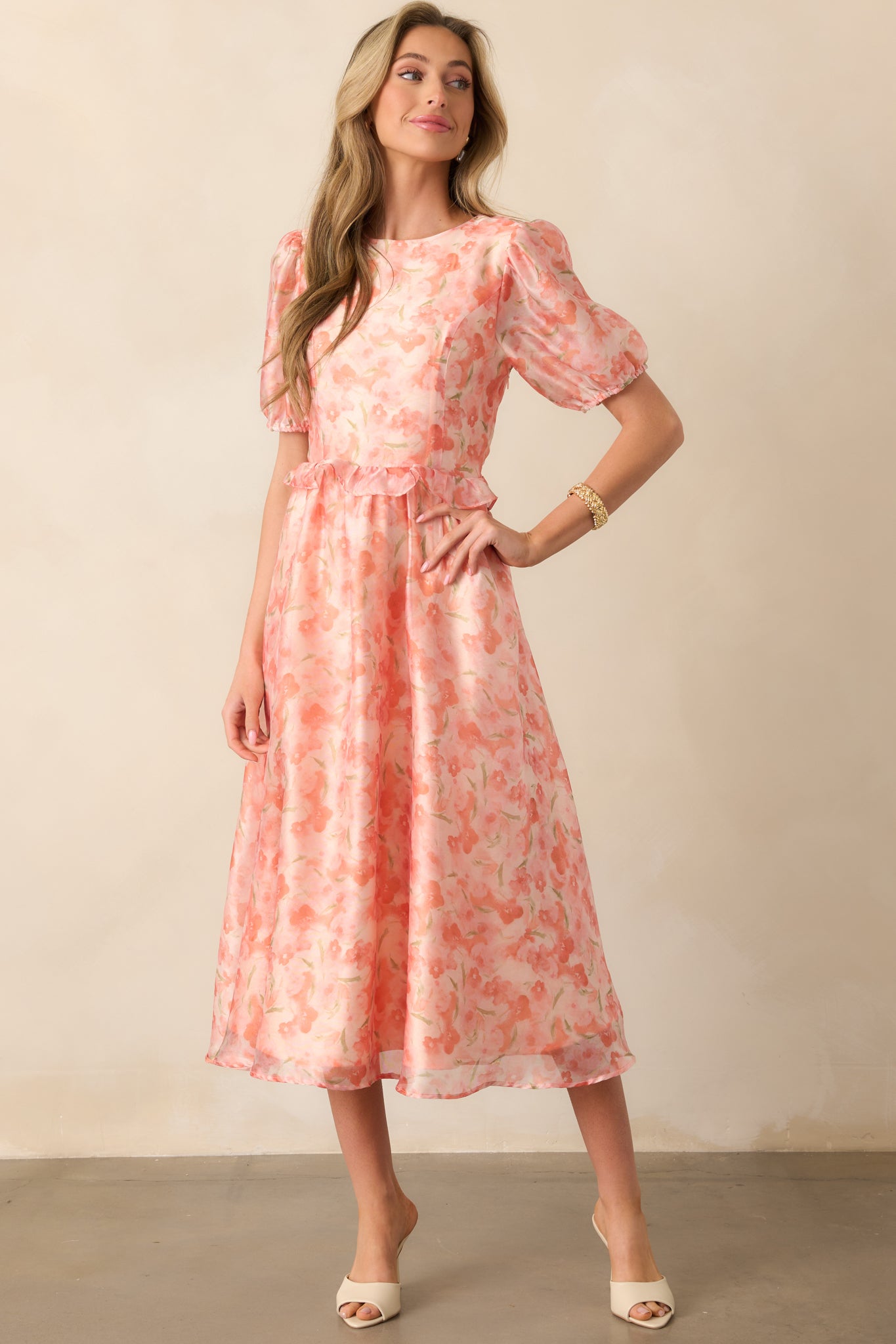A midi dress featuring a soft floral print, puff sleeves with elastic cuffs, and a cinched ruffle waist. The lightweight fabric drapes elegantly.