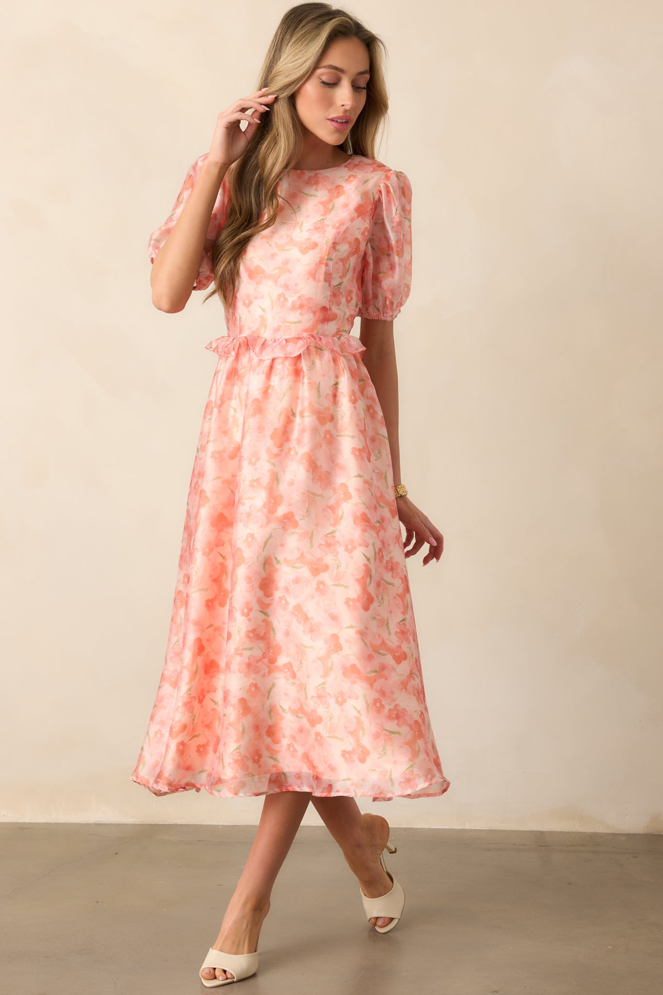 A romantic midi dress with a light orange floral pattern, a round neckline, and subtle puff sleeves. The tiered design and ruffle waist add gentle structure.