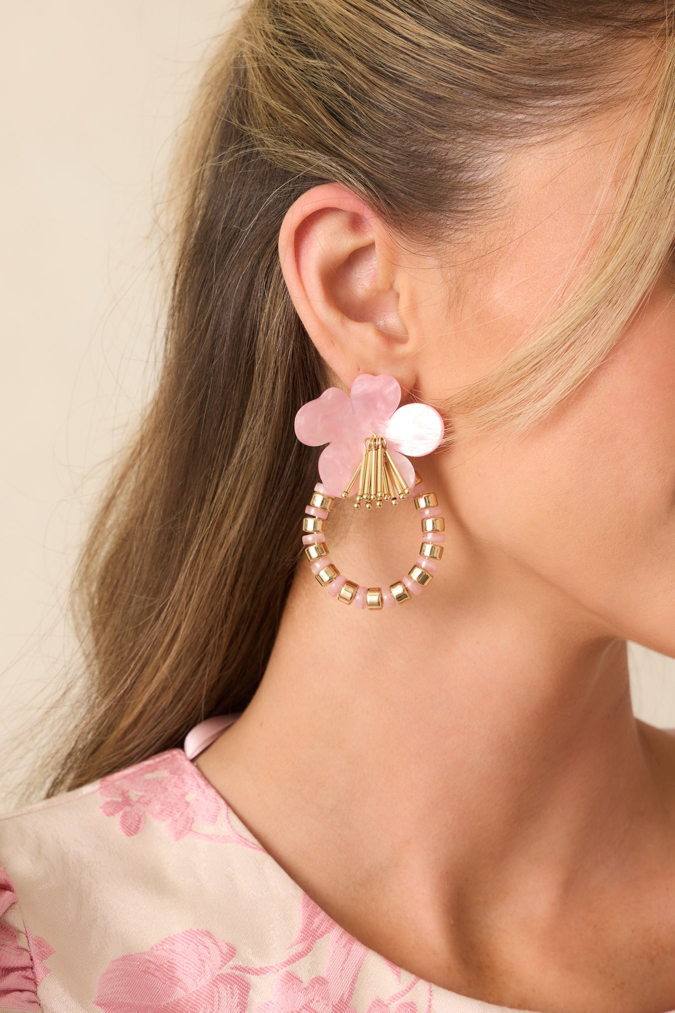 Close-up of a light pink flower earring showing the five rounded pearlescent petals and part of the pink and gold hoop.