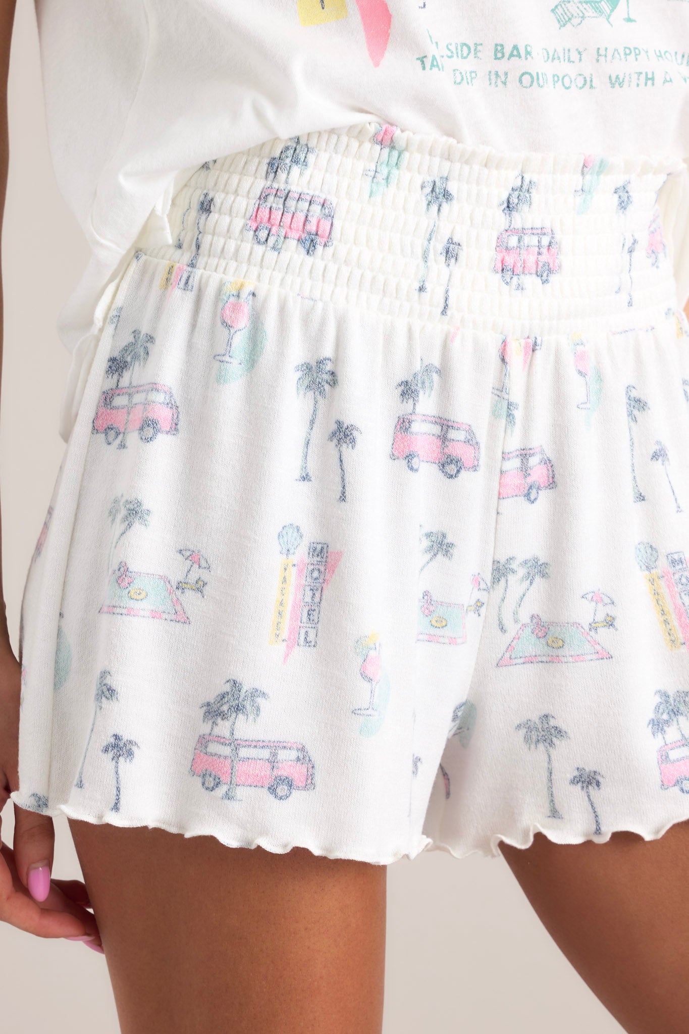 Close up view of these shorts that feature a high waisted design, a fully smocked waistband, a super soft & lightweight material, a tropical print, and a lettuce trim hemline.