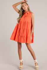 This orange dress features a collared neckline, a full button front, and a tiered design.