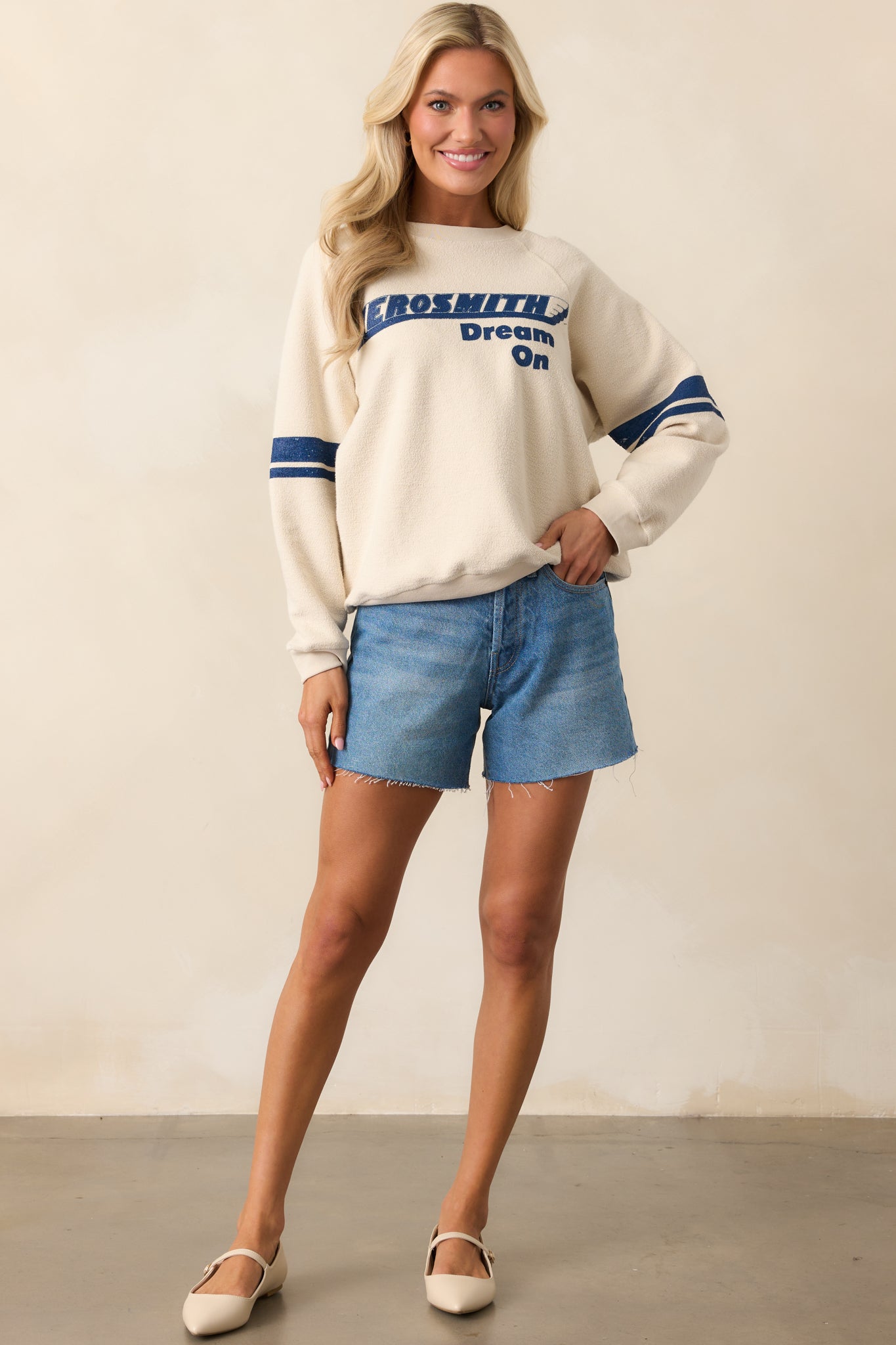 Full body view of ivory sweatshirt featuring textured "Aerosmith Dream On" lettering and blue striped raglan sleeves.