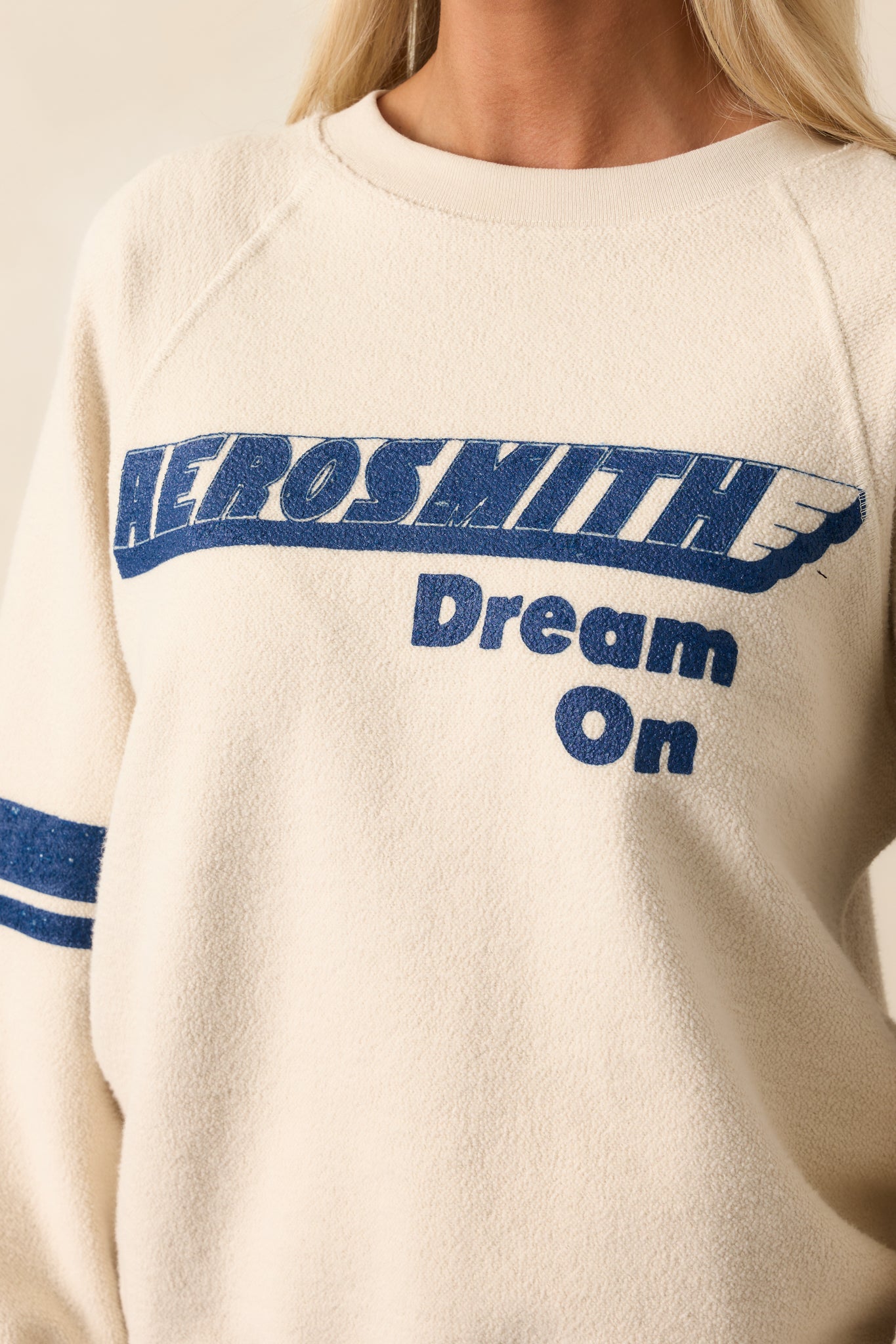 Close-up of textured ivory fabric and raised blue lettering, showing intricate detail of the front graphic.