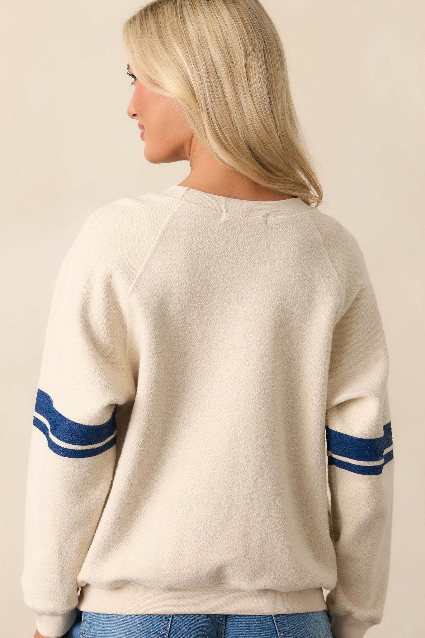 Rear view of sweatshirt featuring ivory textured fabric, raglan seam lines, and blue-striped sleeves continuing to the back.
