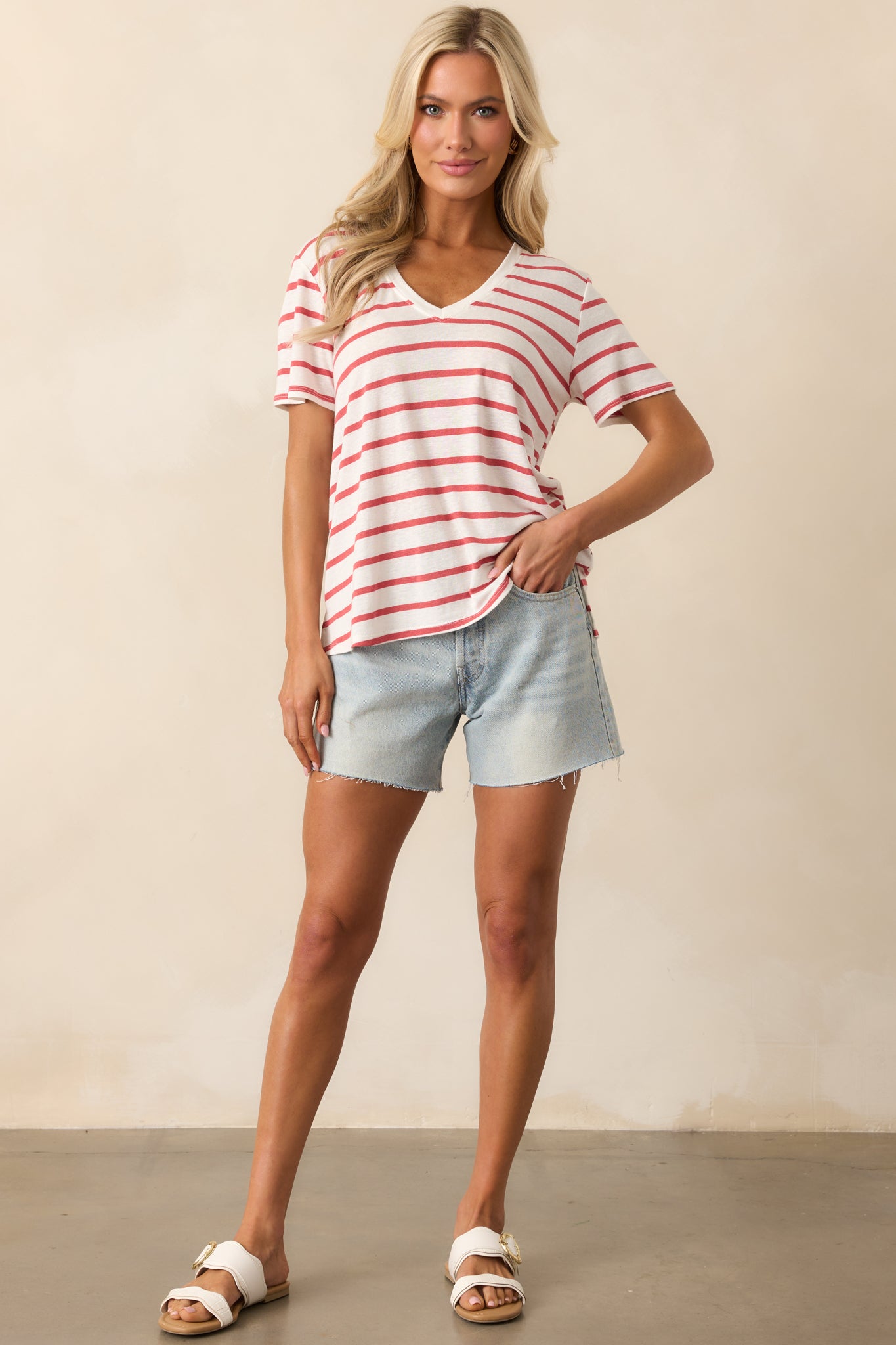 Front view of the light red and white striped top, showcasing the v-neckline, short sleeves, and split bottom hem, creating a laid-back, stylish look.