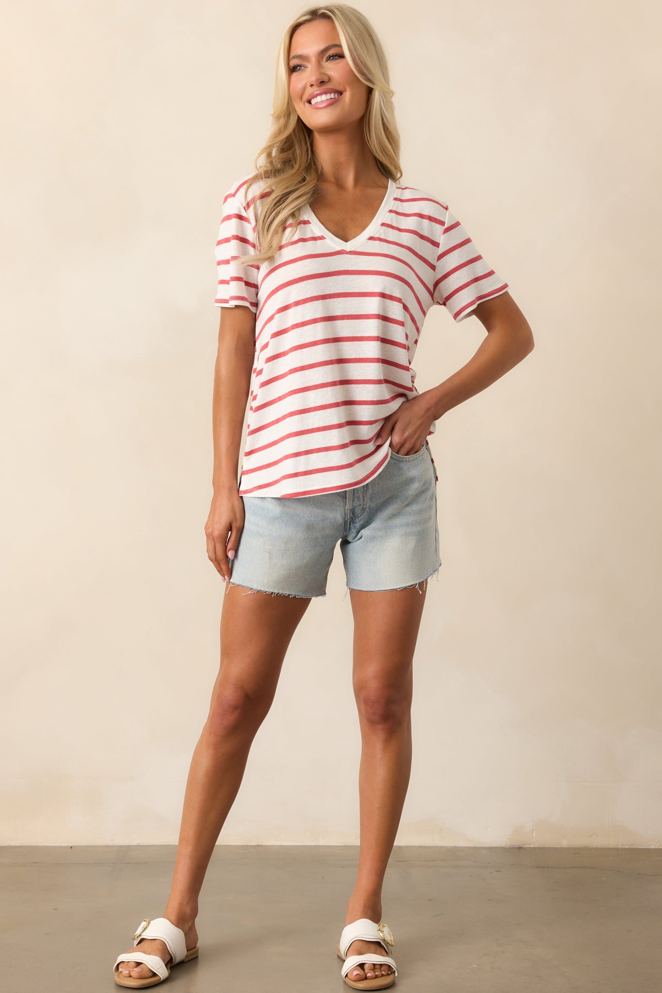 A full-body shot of the relaxed-fit top in light red and white stripes, featuring a v-neckline and short sleeves, with a split bottom hem adding a touch of modern flair.