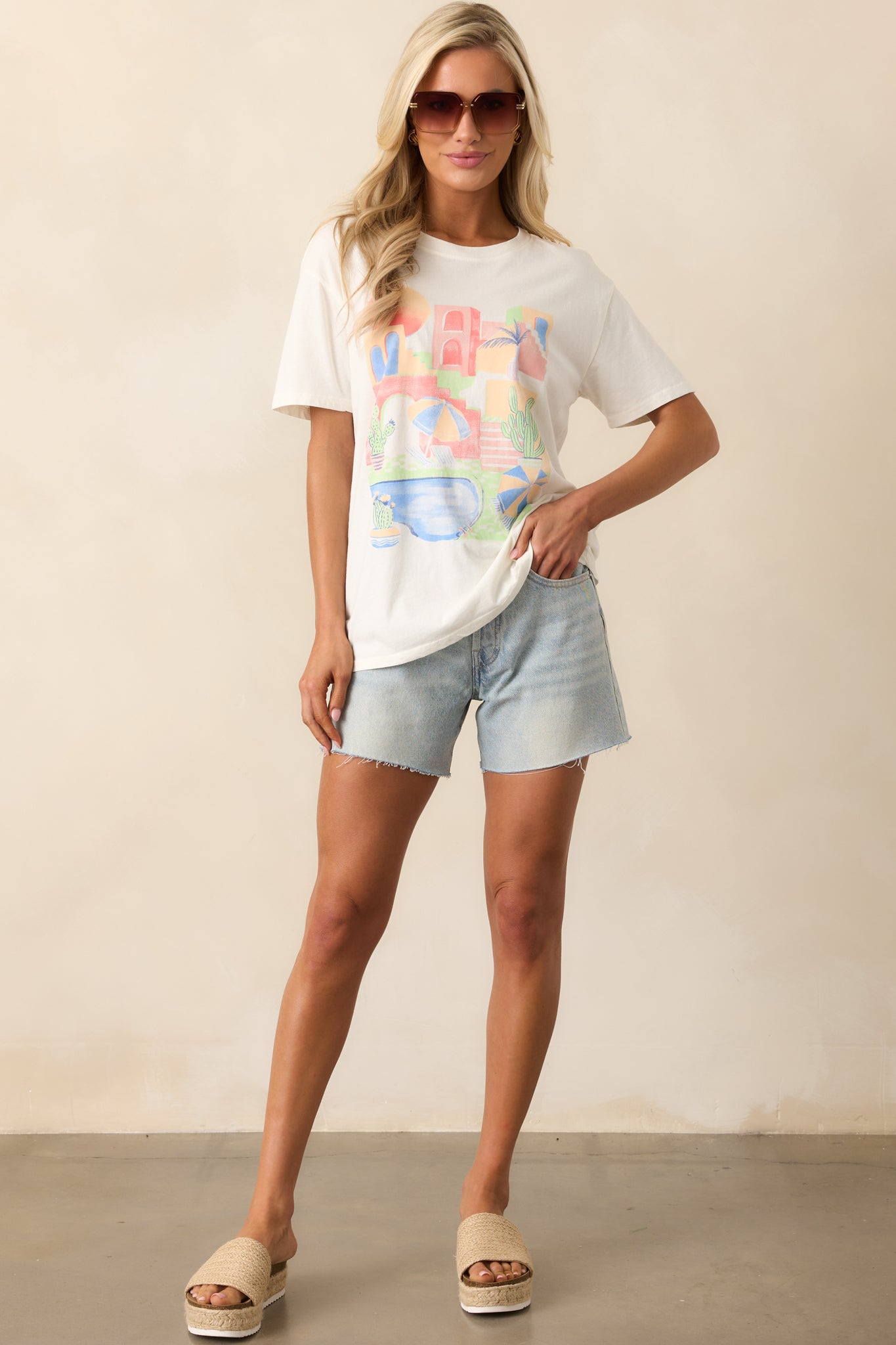An ivory top with a beautiful beach graphic, complemented by a crew neckline and short sleeves. The relaxed fit creates a breezy, casual look.