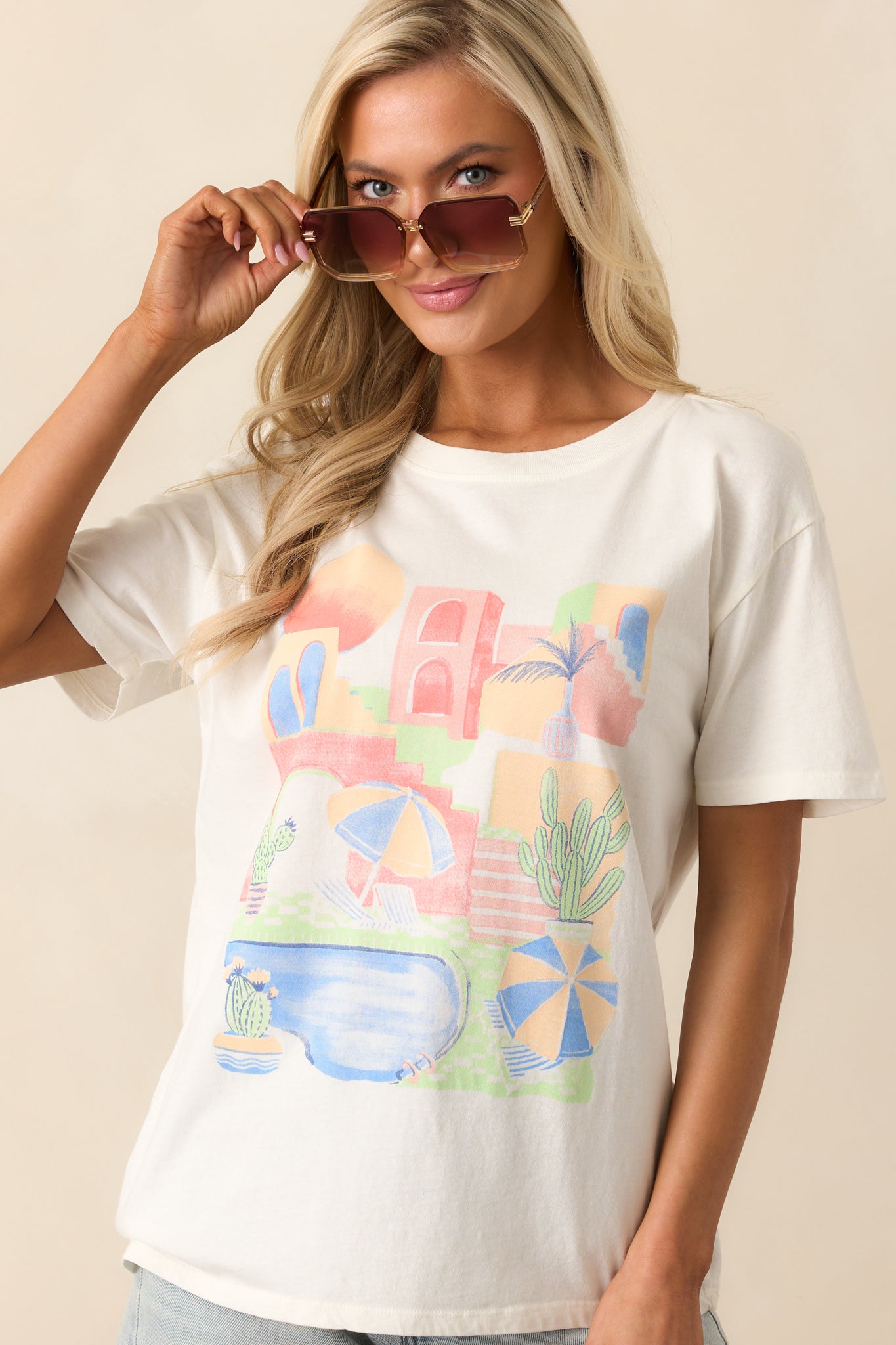 This ivory top features a scenic beach graphic on the front, a crew neckline, and short sleeves. The relaxed fit ensures comfort and a laid-back style.