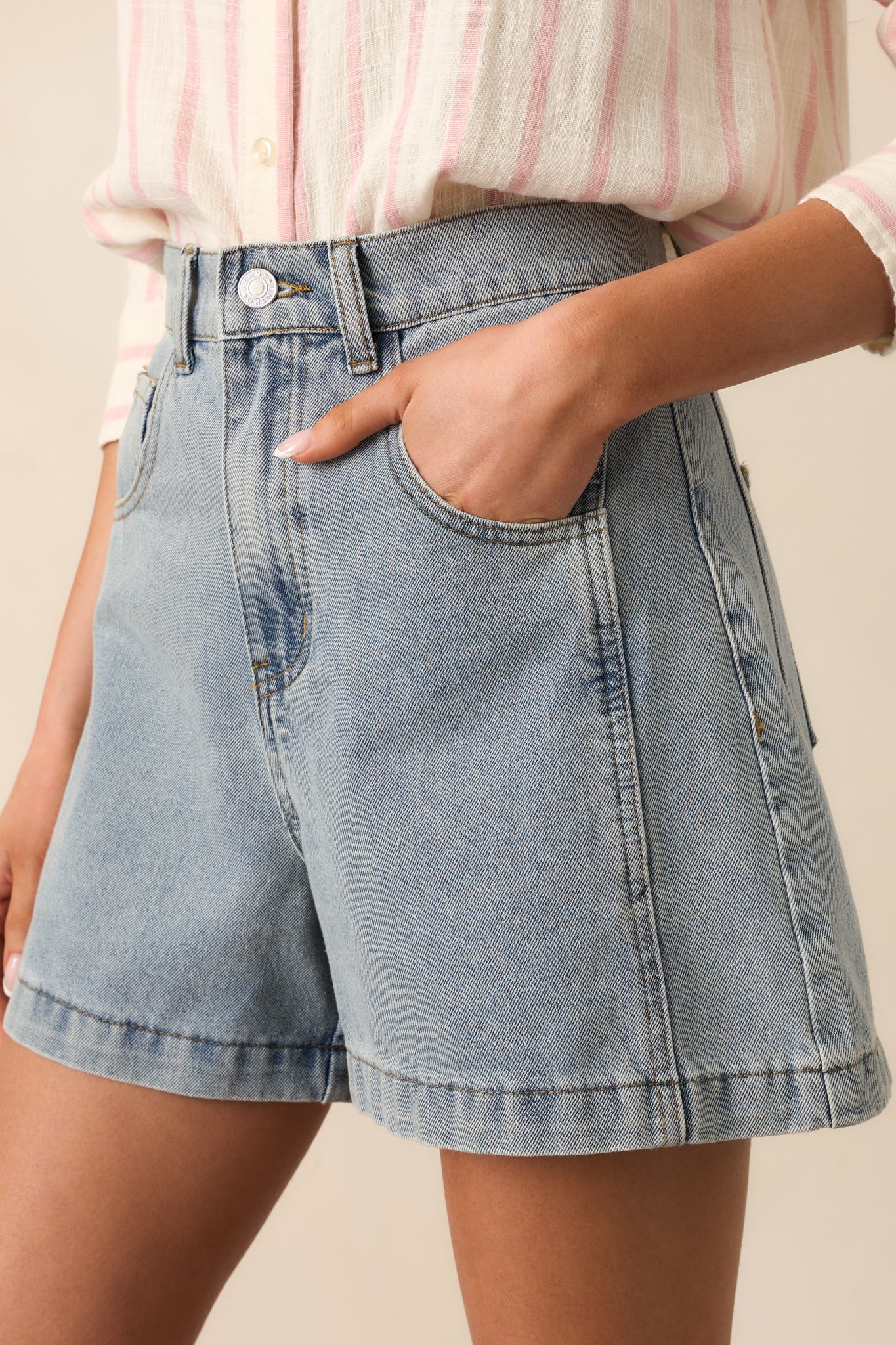 A close-up of the classic button and zipper closure on these light wash denim shorts, made from durable 100% cotton fabric with functional pockets for added convenience.