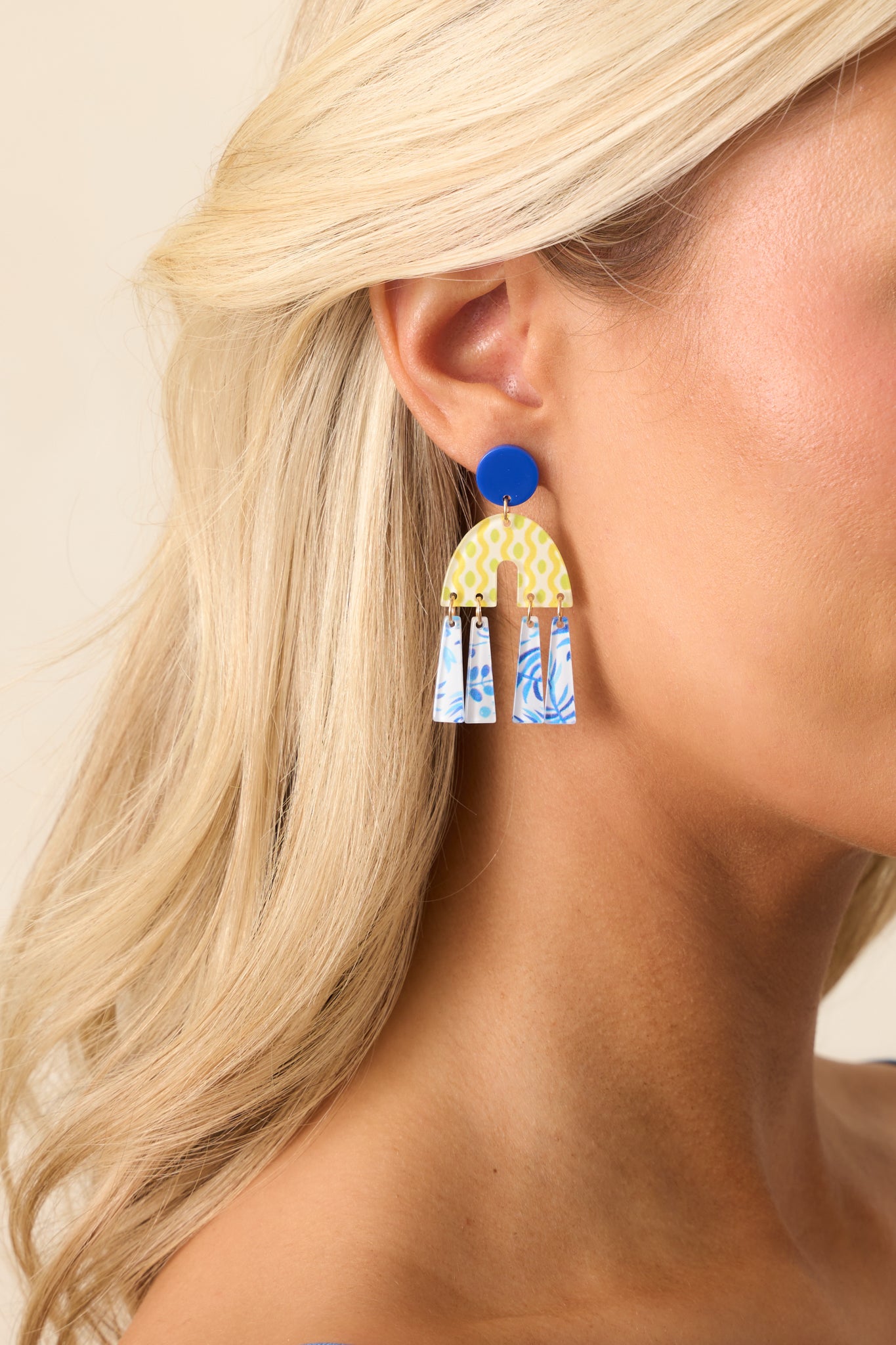 A zoomed-in shot of the blue earrings, highlighting the layered geometric drop charms in yellow and blue, paired with a circular blue stud for a playful, statement-making style.