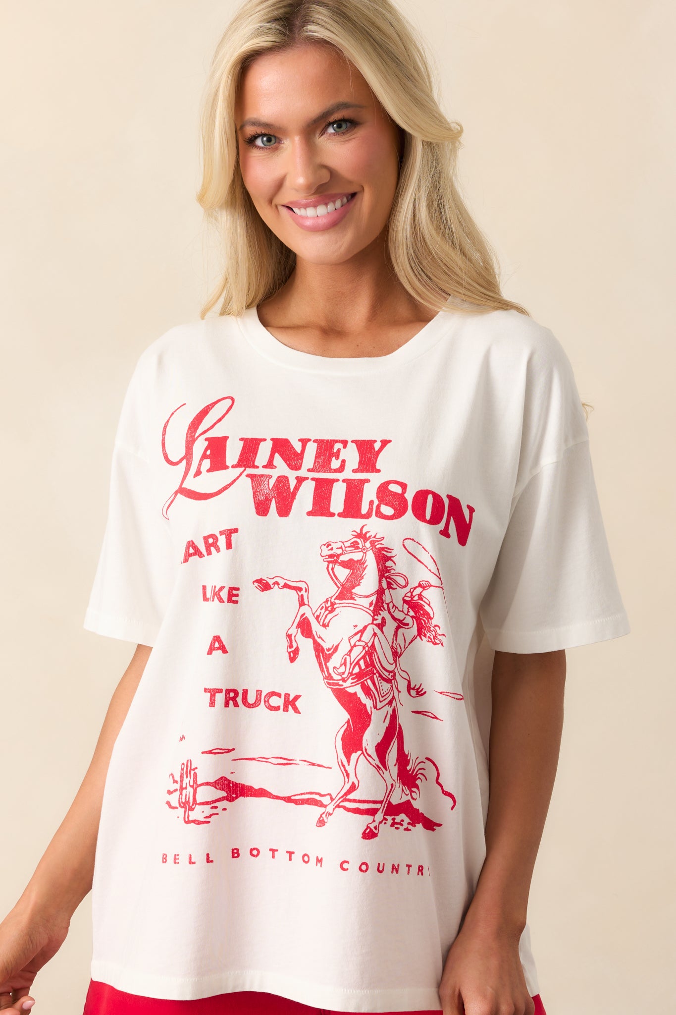 A full view of the white tee featuring a crew neckline, short sleeves, and an oversized fit, with a bold red "Lainey Wilson Heart Like A Truck" printed graphic on the front.