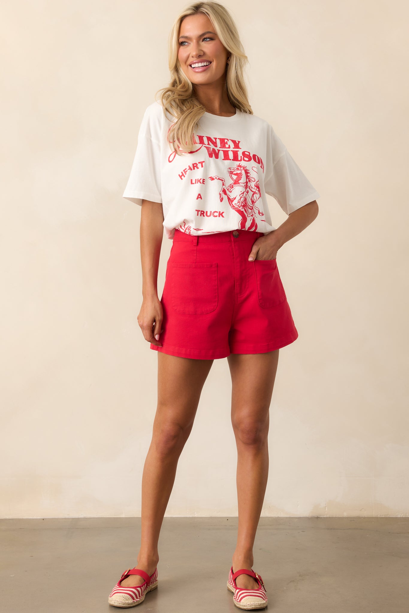 A front-facing view of the red shorts, showcasing the high-waisted silhouette, functional front patch pockets, and tortoise shell button closure, with belt loops adding a classic touch.