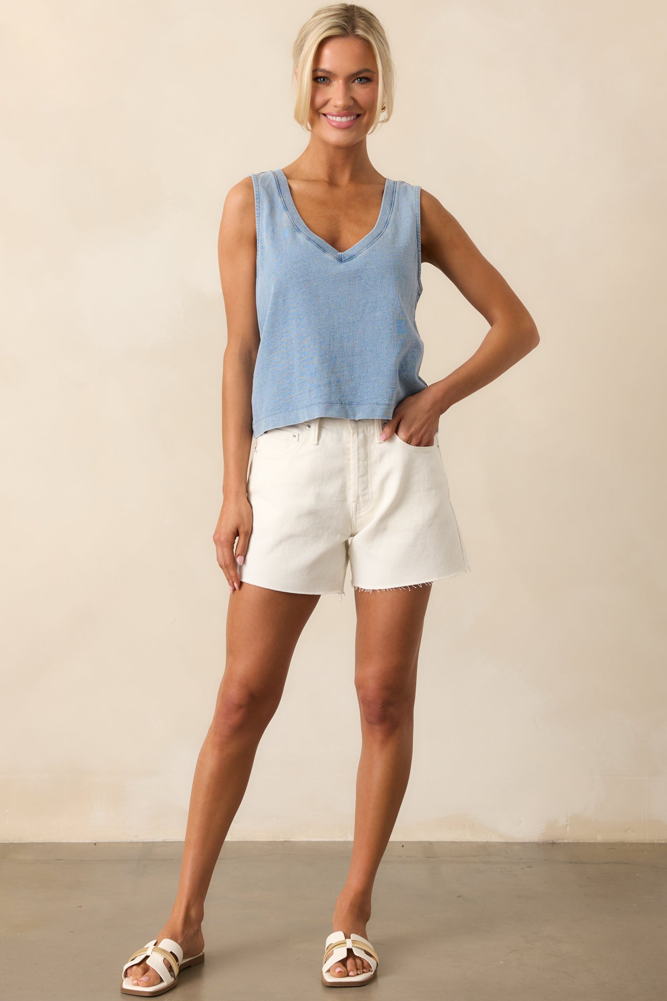 Full body view of these white shorts that feature a high waisted design, a classic button & zipper closure, belt loops, functional front & back pockets, and a raw hemline.