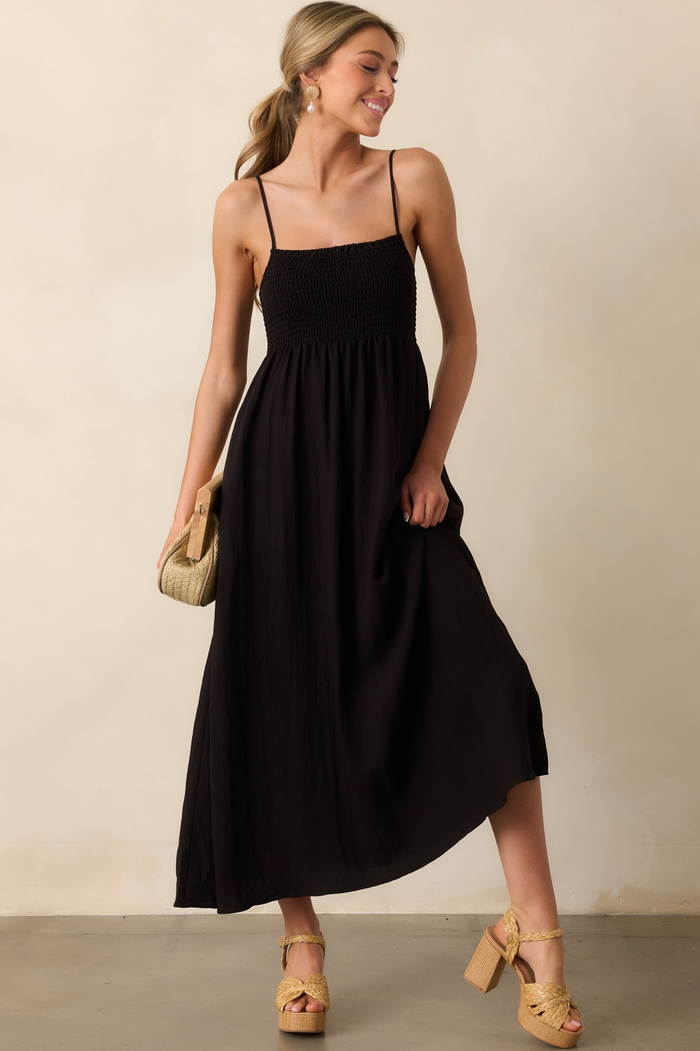 Front view of black midaxi dress featuring smocked bust, functional pockets, and a flowy skirt that reaches mid-calf.