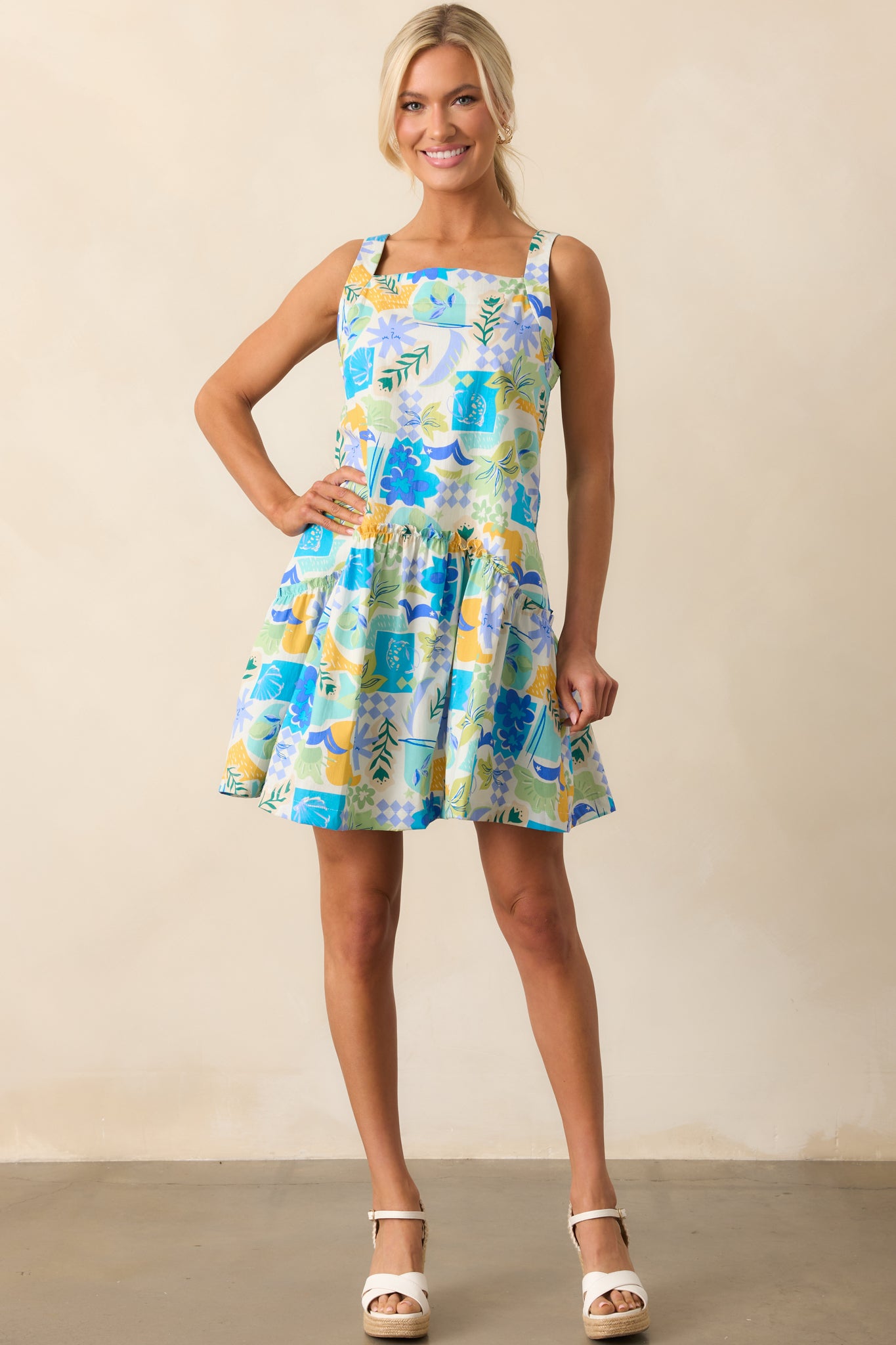 A statement mini dress in bright blue with a lively tropical print, finished with a high square neckline and a flowing silhouette.