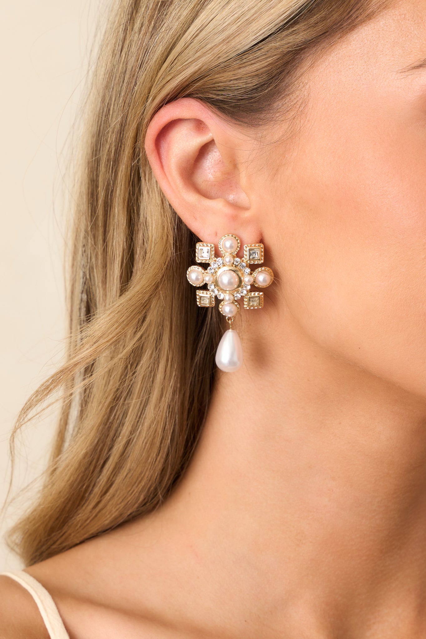 View of one earring showing the faux ivory pearl center framed by tiny pearls and faux diamonds with a teardrop pearl dangle.