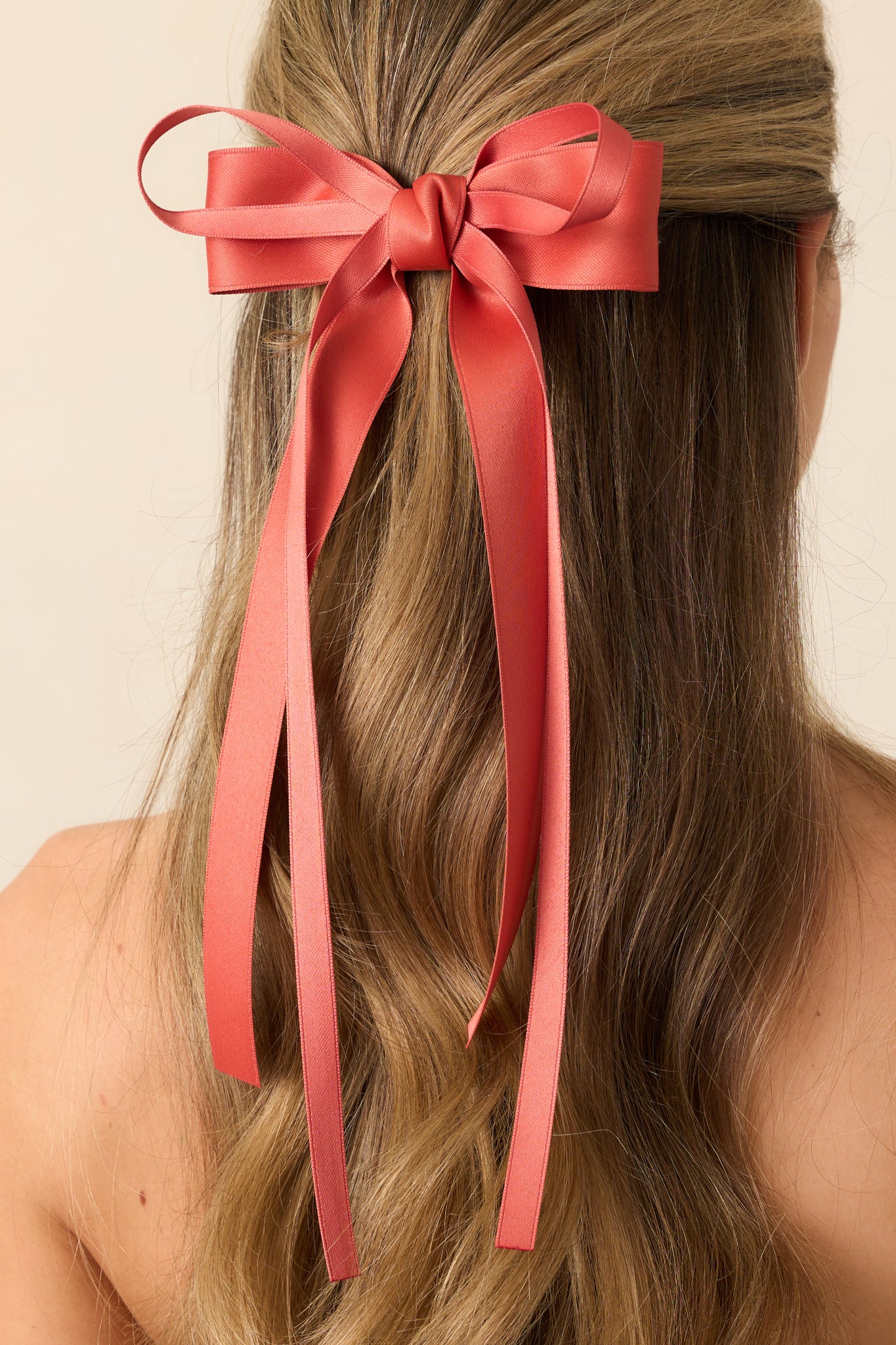Close up of this orange clip in bow featuring a layered bow design, a thick orange bow bottom layer and a thin ribbon bow layered on top, long tails on each bow, and a barrette clip.