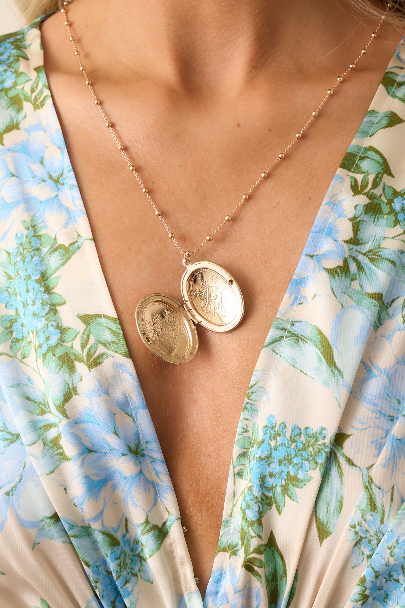 Opened up angle of the necklace highlighting the functional locket along the chain and the engraved pattern on the gold oval locket.