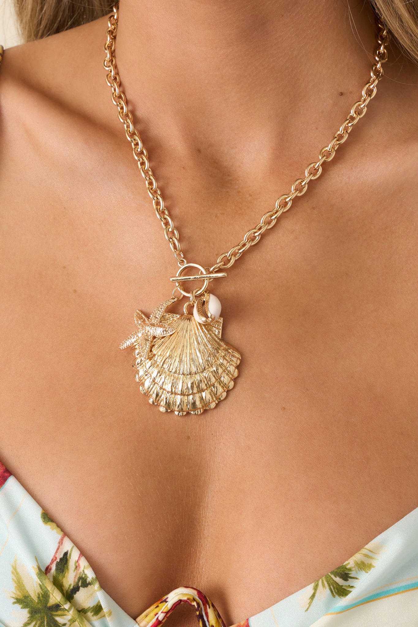 Close-up of a gold charm necklace highlighting the textured shell and starfish charms, bead details, and toggle closure.