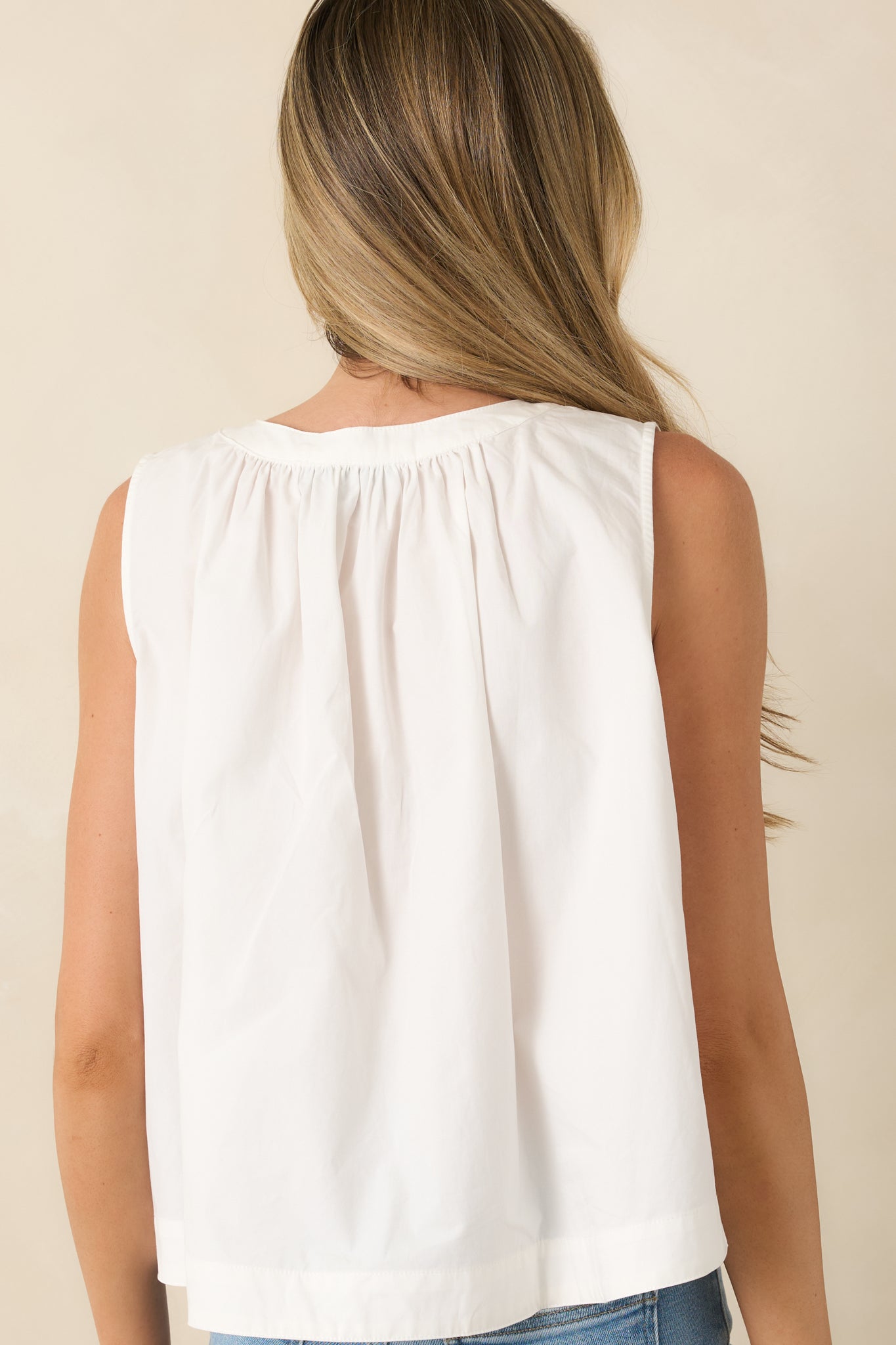 Rear view of the white sleeveless blouse featuring a relaxed drape and lightweight cotton construction.