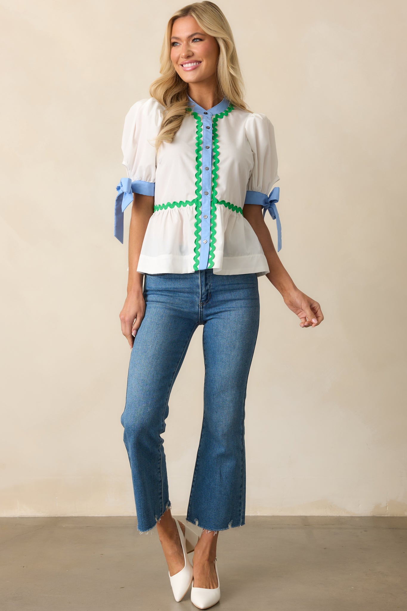 Ivory top with puff sleeves, blue self-tie cuffs, and a button front design, featuring green ric rac piping along the neckline.