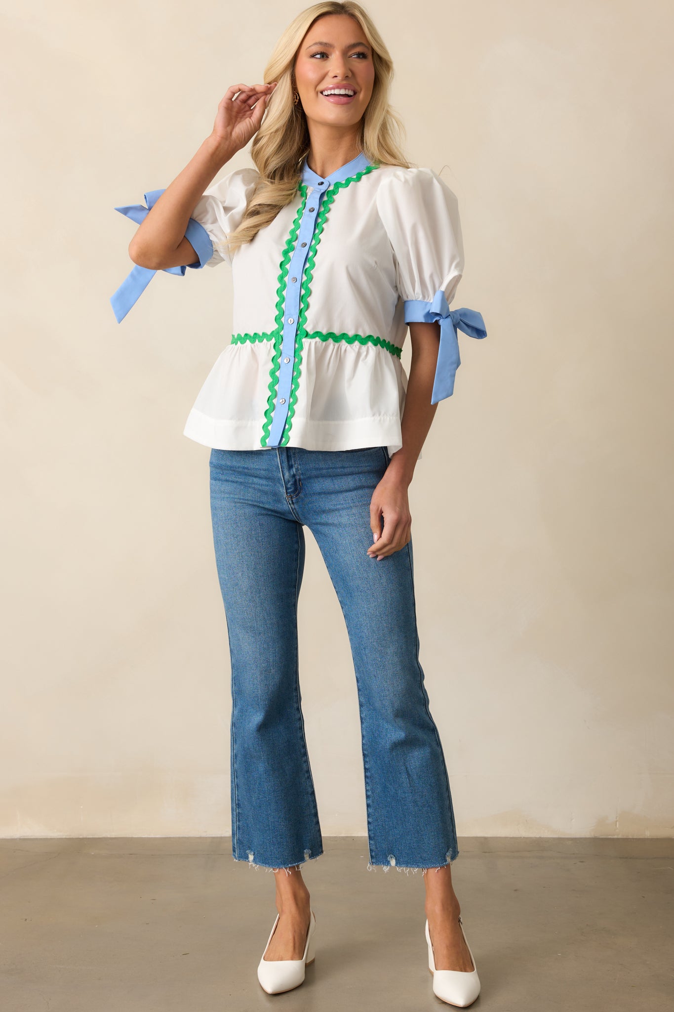 Ivory puff sleeve top featuring a round neckline, peplum silhouette, and decorative blue self-tie cuffs with ric rac piping.