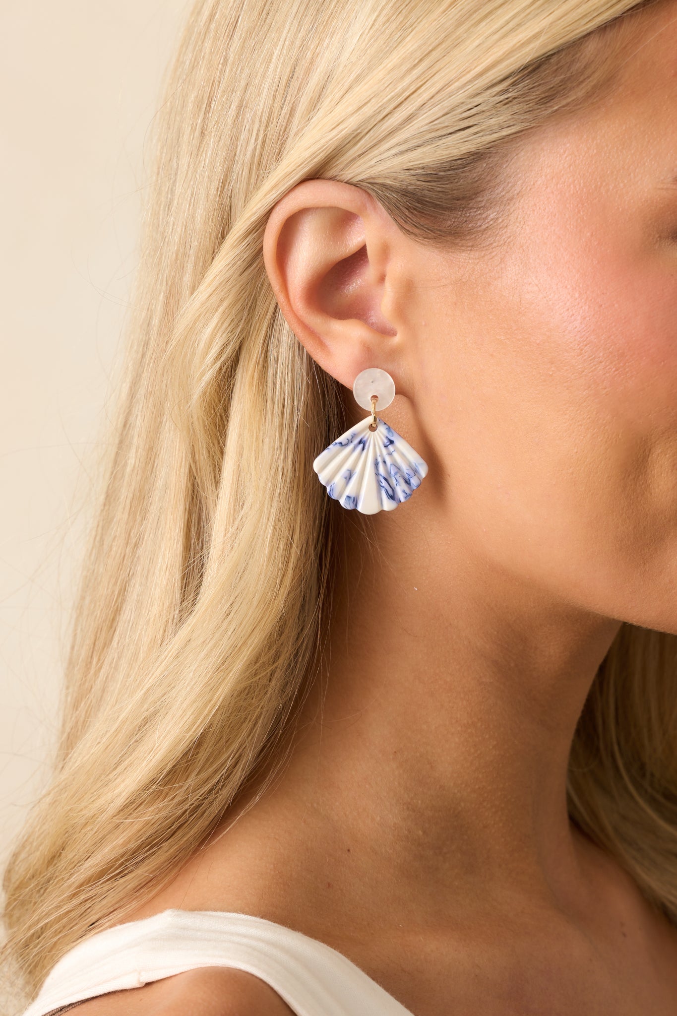 Close-up cropped view of the earrings highlighting the ivory pearlescent circular stud and gold jump rings connecting to the seashell drop.
