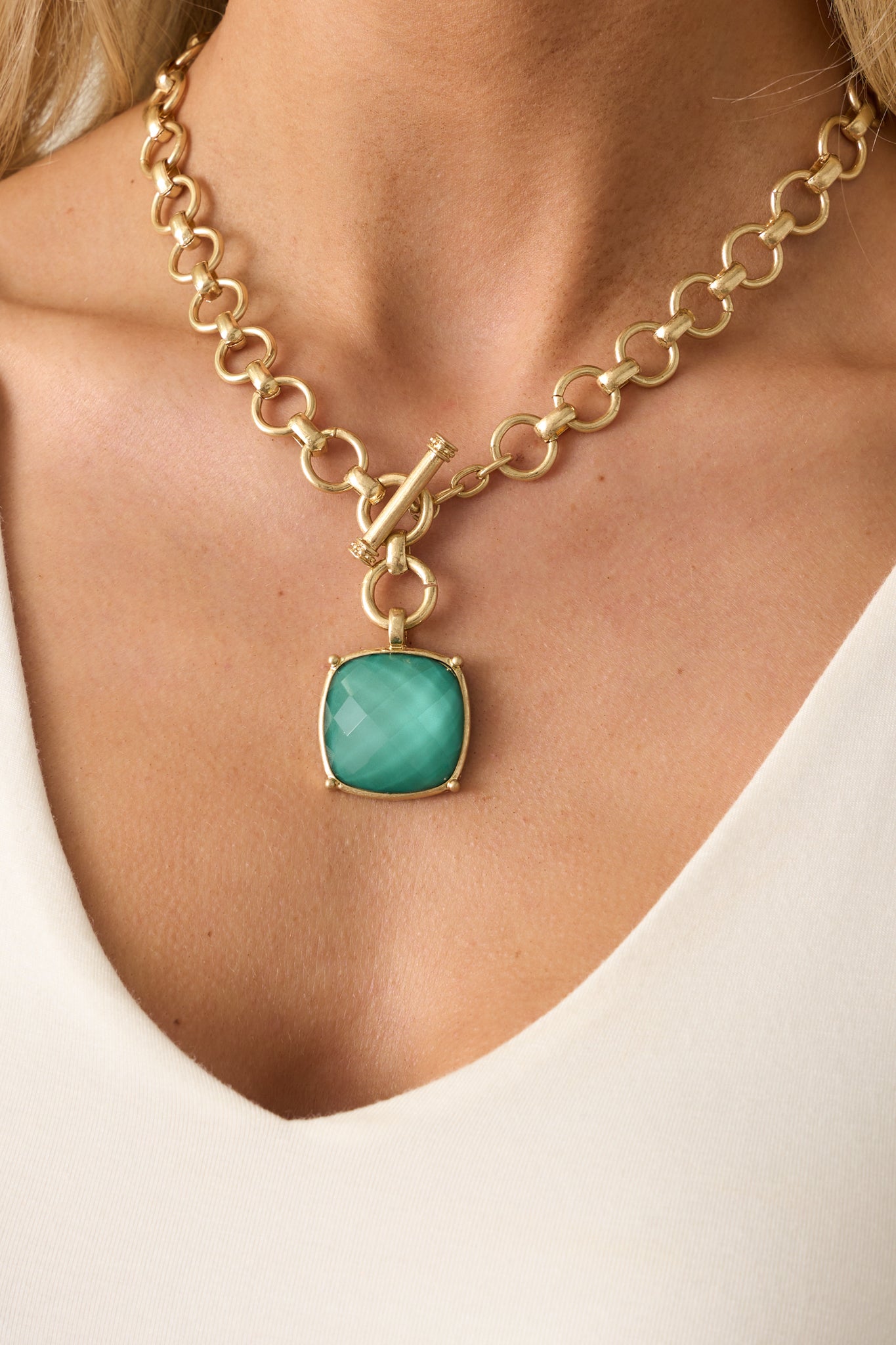 Tightly framed image highlighting the front toggle clasp closure and the textured gold setting around the green stone.