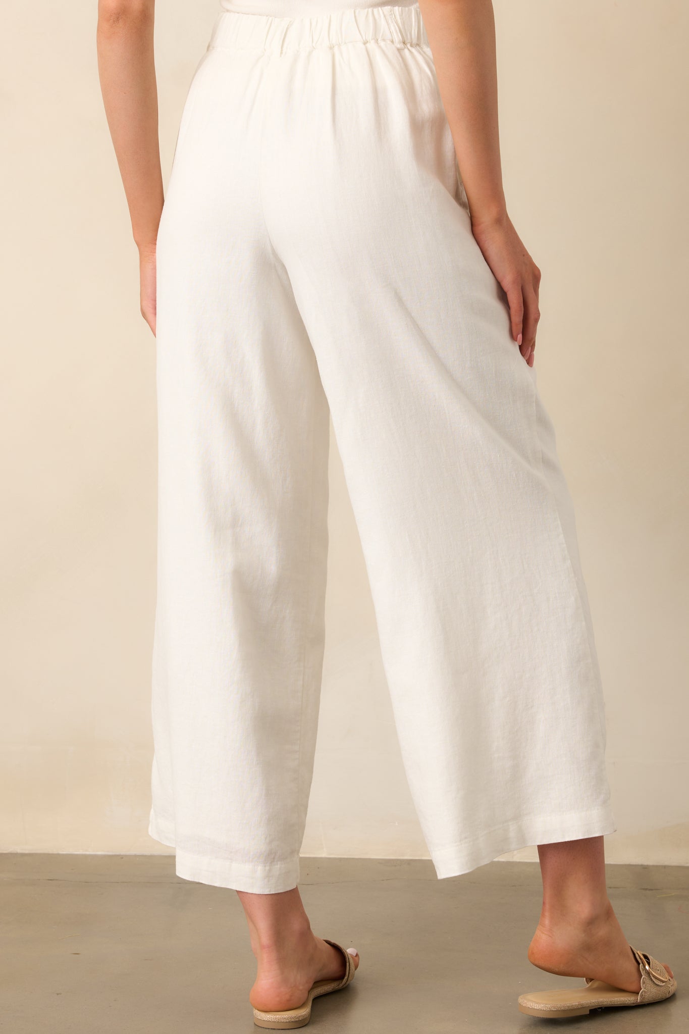 A view from behind of the white linen pants, highlighting the elastic waistband insert and functional pockets.