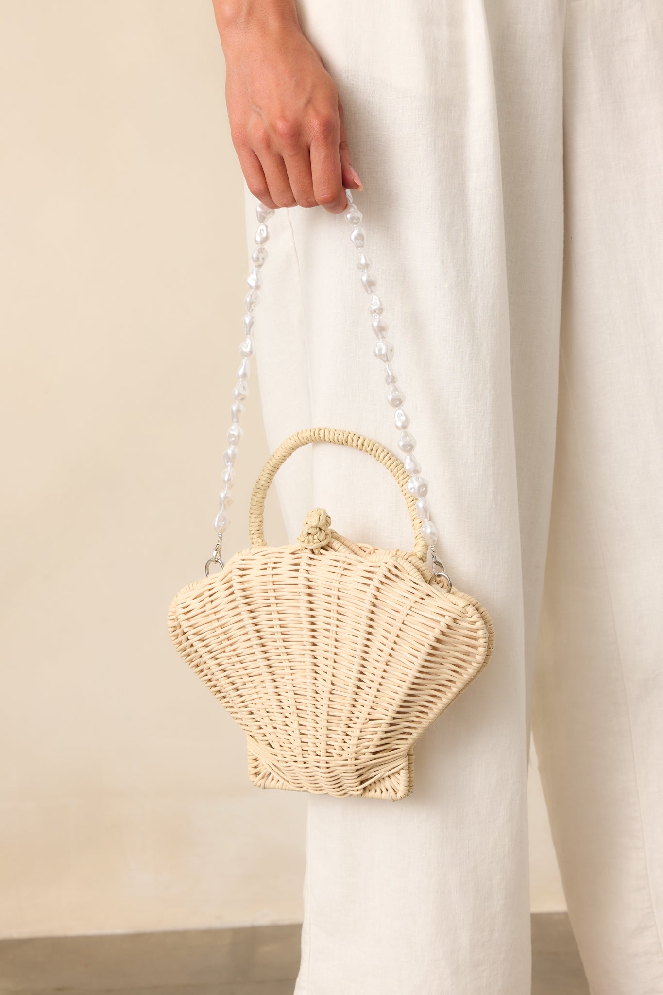 Ivory rattan handbag with a woven handle and pearl shoulder strap displayed against a neutral backdrop, showcasing the full structured silhouette.