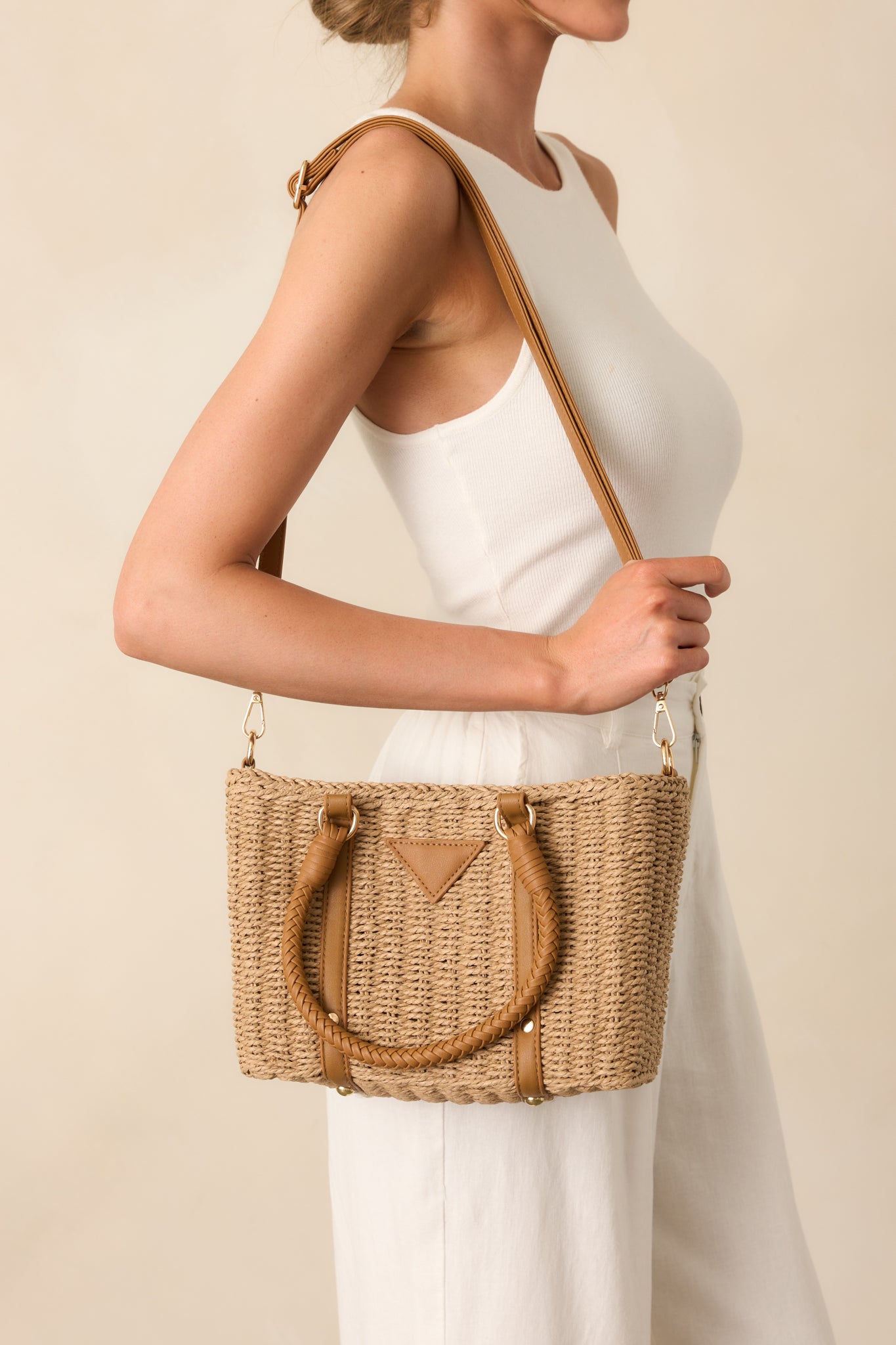 The tan rattan handbag styled with an optional faux leather crossbody strap, showcasing its structured silhouette and woven handles.